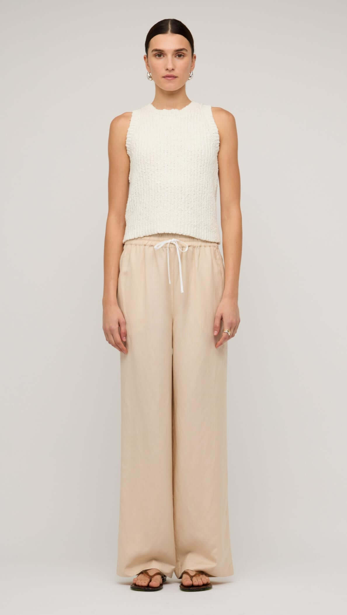 Woman wearing beige relaxed linen wide-leg pants paired with a cream knitted tank top.