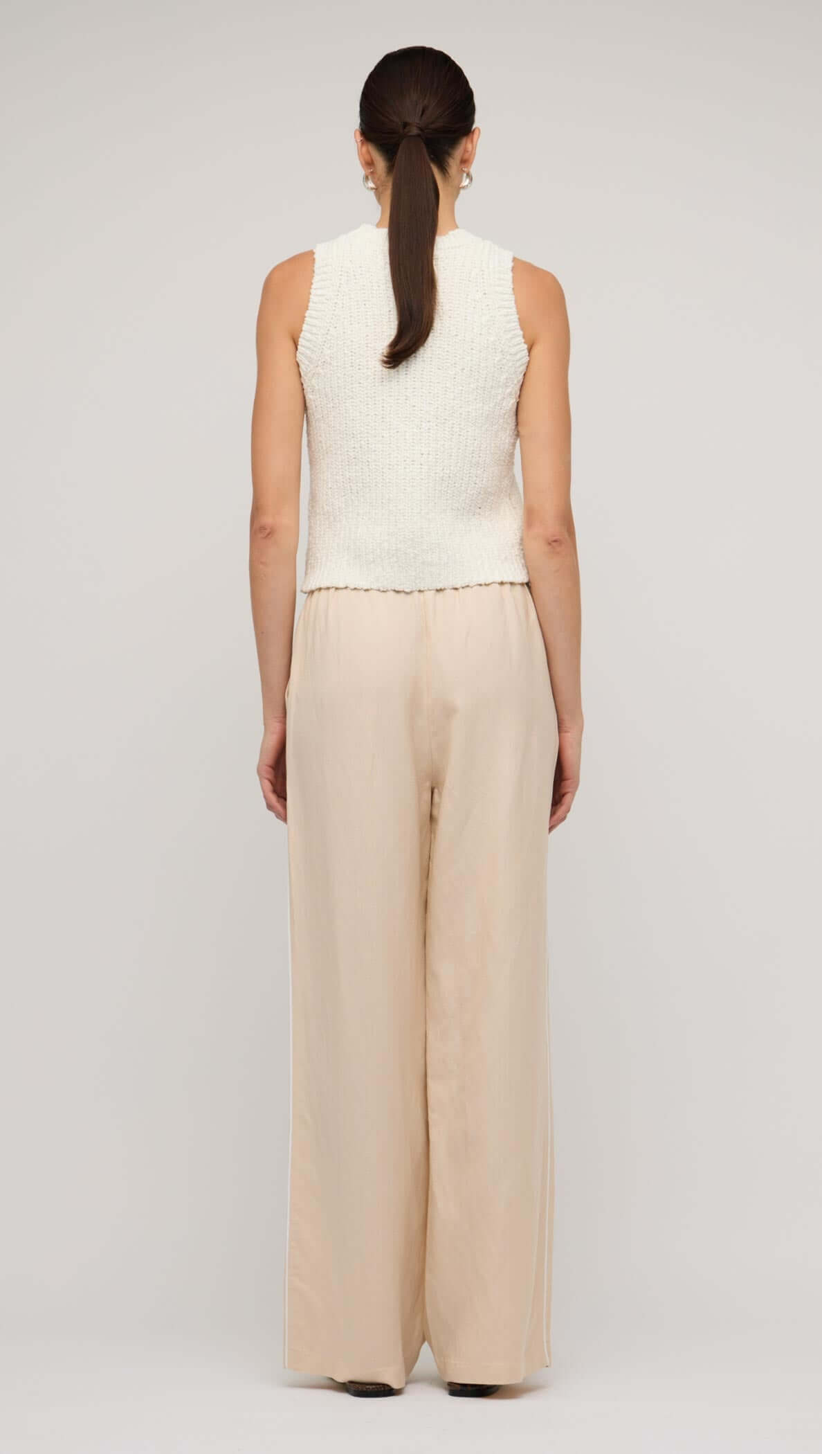 Back view of a woman wearing relaxed beige linen wide-leg pants with a sleeveless knitted top.