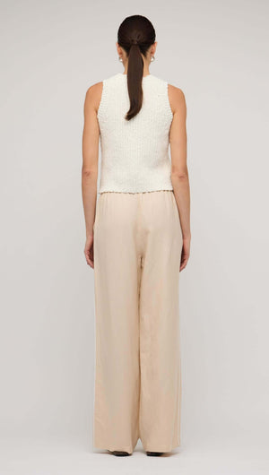 Back view of a woman wearing relaxed beige linen wide-leg pants with a sleeveless knitted top.