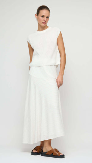 Model wearing an Asymmetric White Bias Maxi Skirt paired with a white top, showcasing a fluid silhouette.