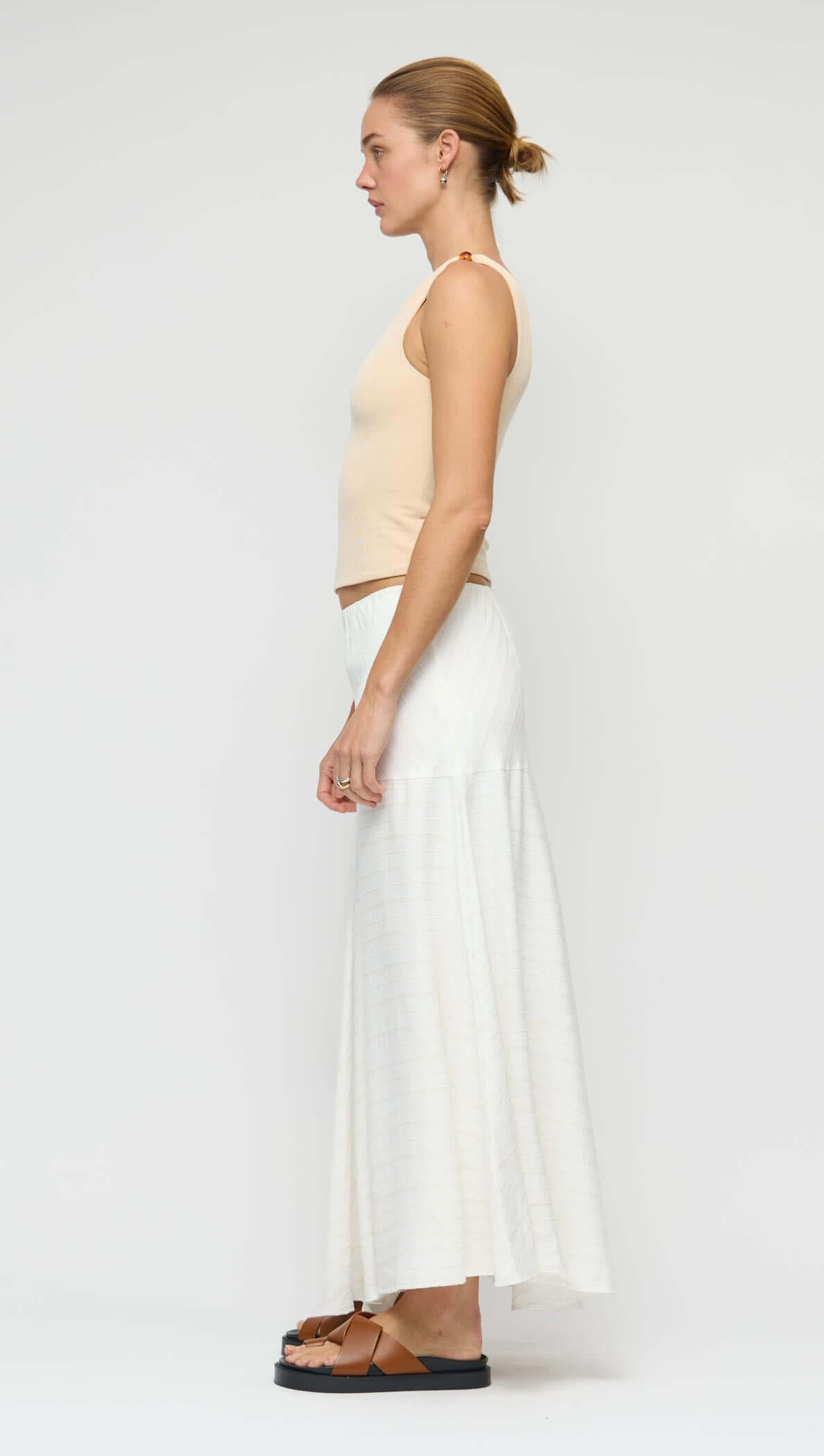 Model showcasing the Asymmetric White Bias Maxi Skirt from the side, highlighting its fluid silhouette and design.