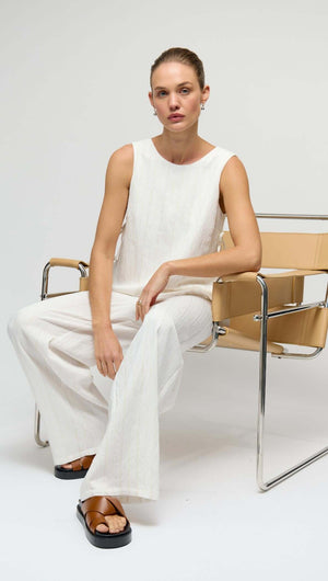 Model wearing a White Tie-Side Top, seated on a chair, showcasing a minimal summer style with relaxed tailoring.