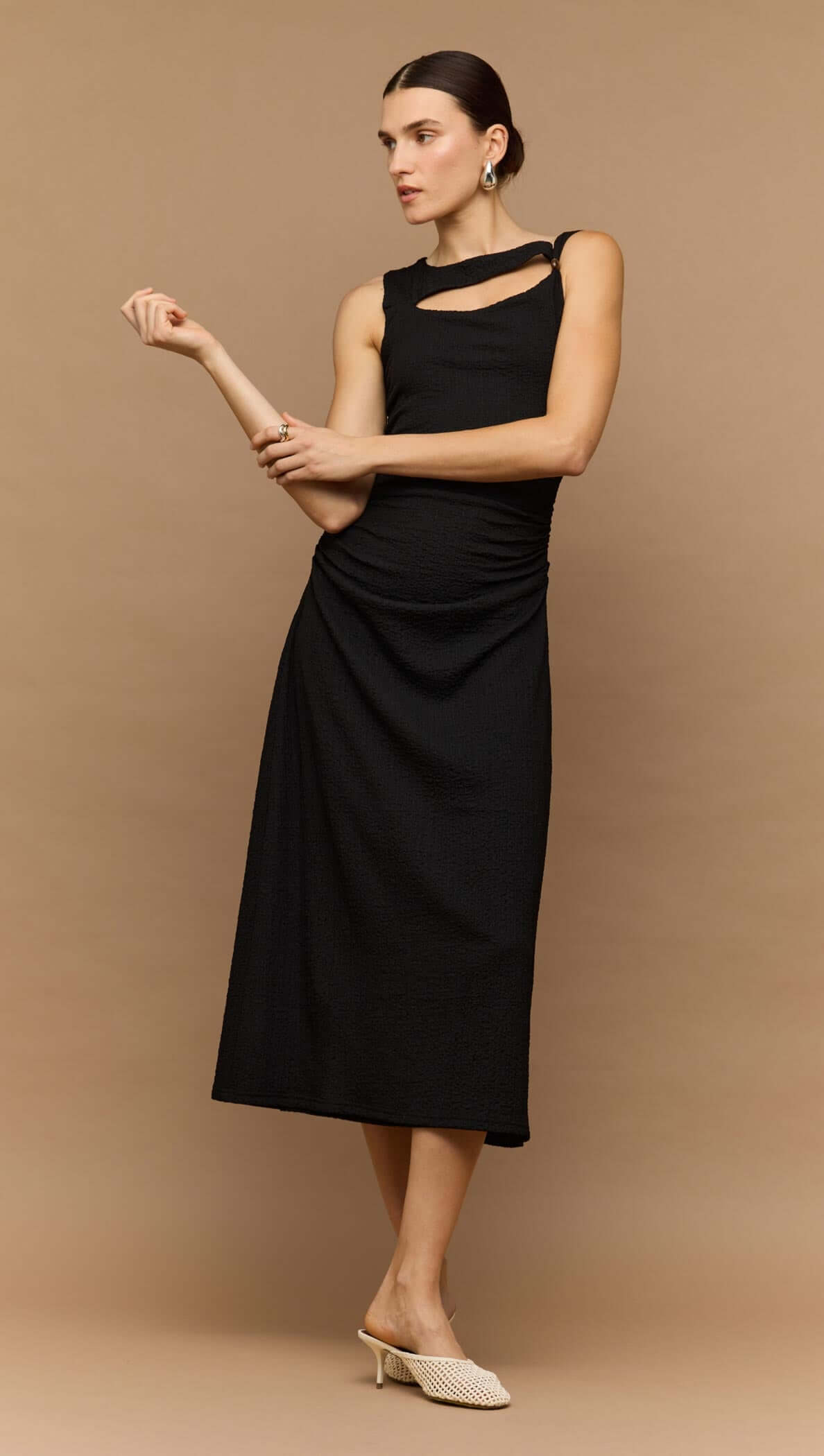 Model wearing a black cut out ruched A-line midi dress with bead detail, showcasing a sleek and sophisticated look.