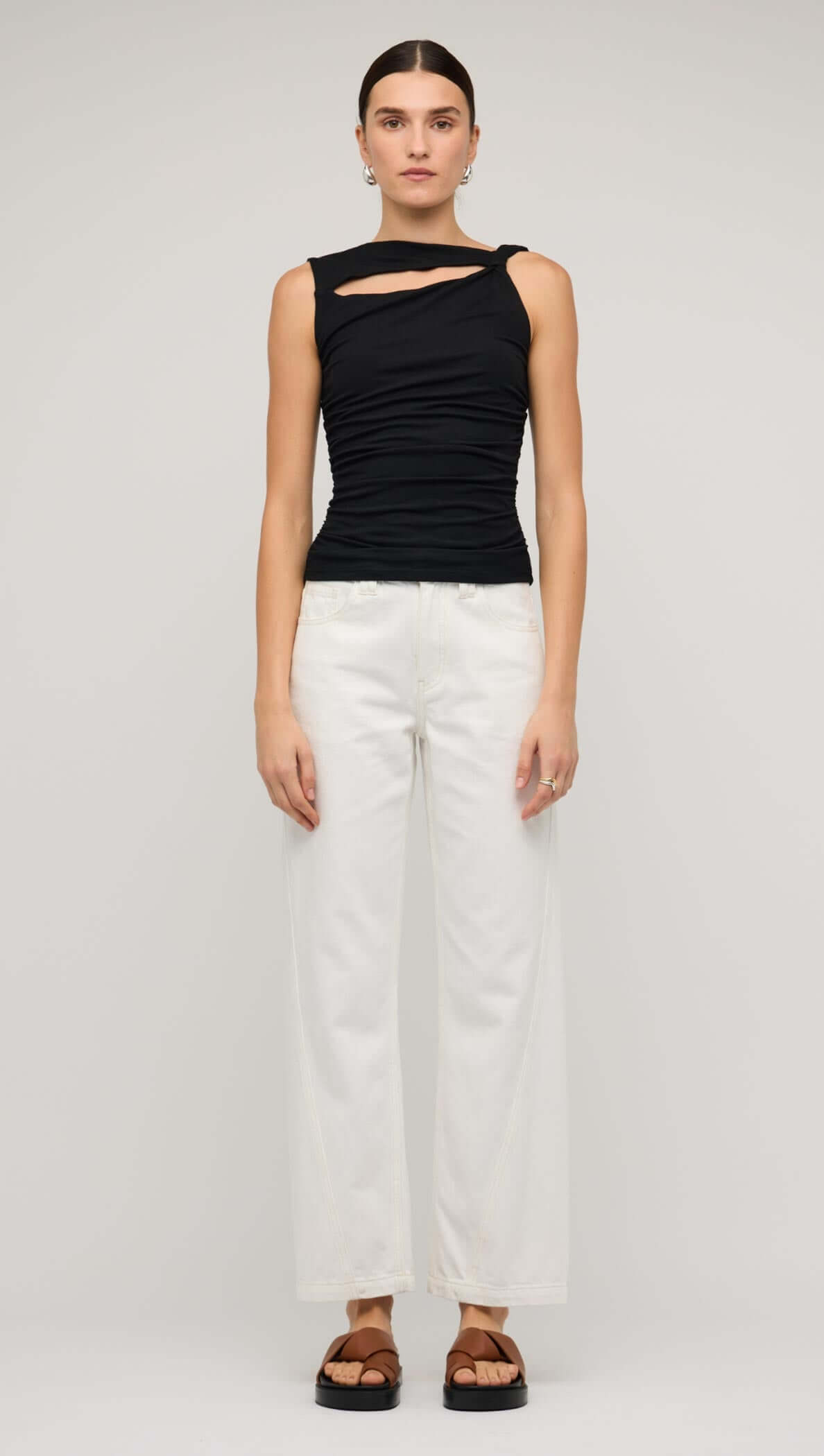 Model wearing a black cut out ruched top with bead detail, paired with white wide-leg pants and black sandals.