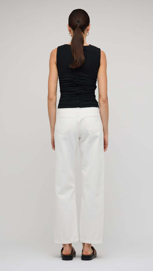 Model showing the back view of a black cut out ruched top paired with white wide-leg pants.