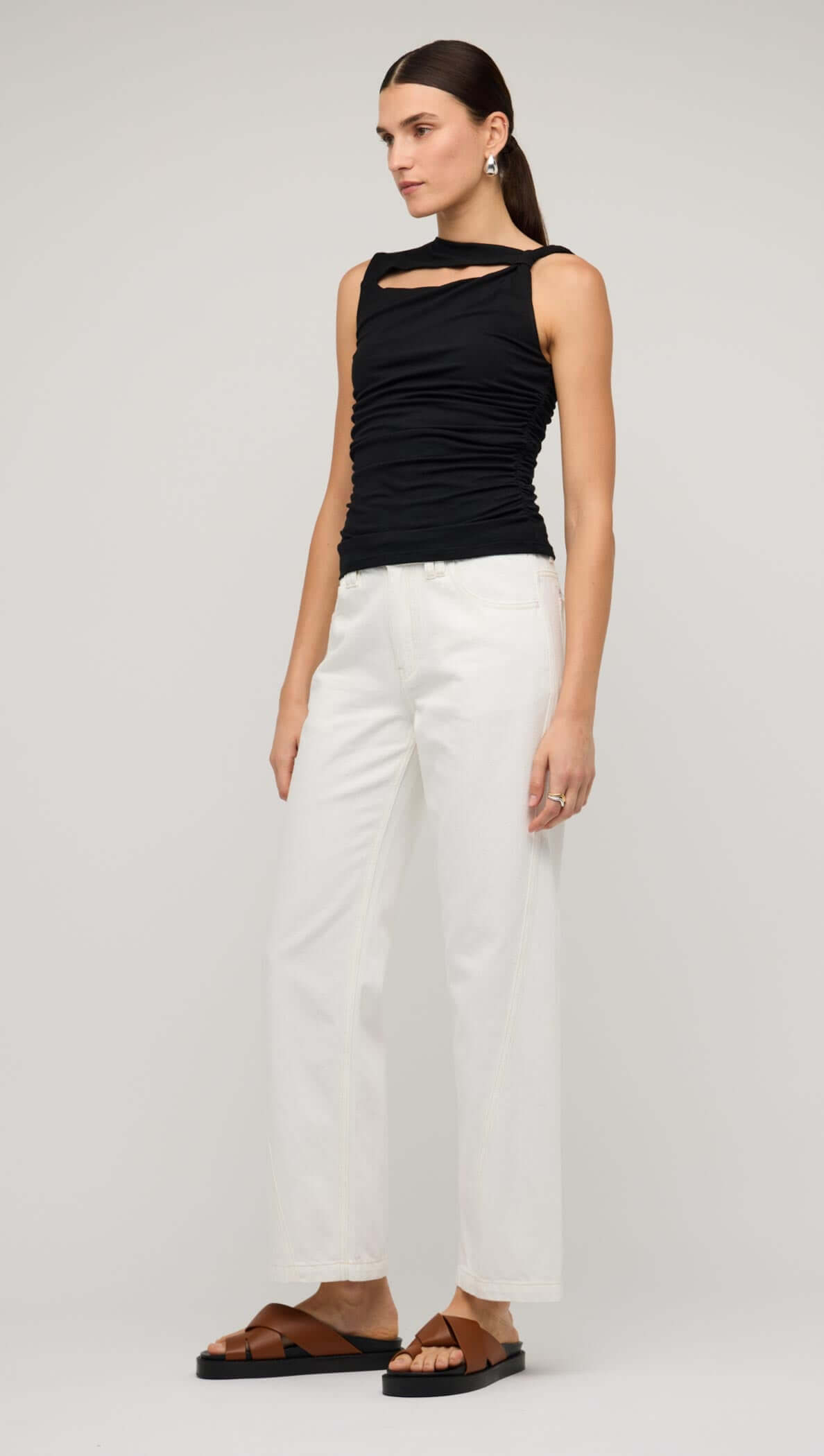 Model wearing a black cut out ruched top with bead detail paired with white pants and sandals.