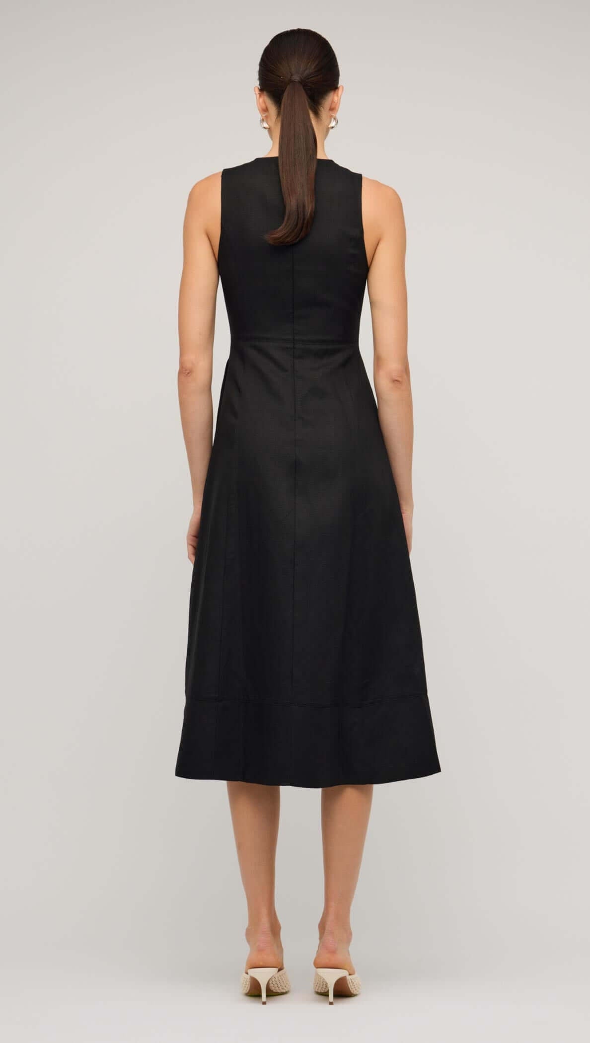 Black linen A-line midi dress with sleeveless design and subtle pleats, modeled by a woman on a neutral background.