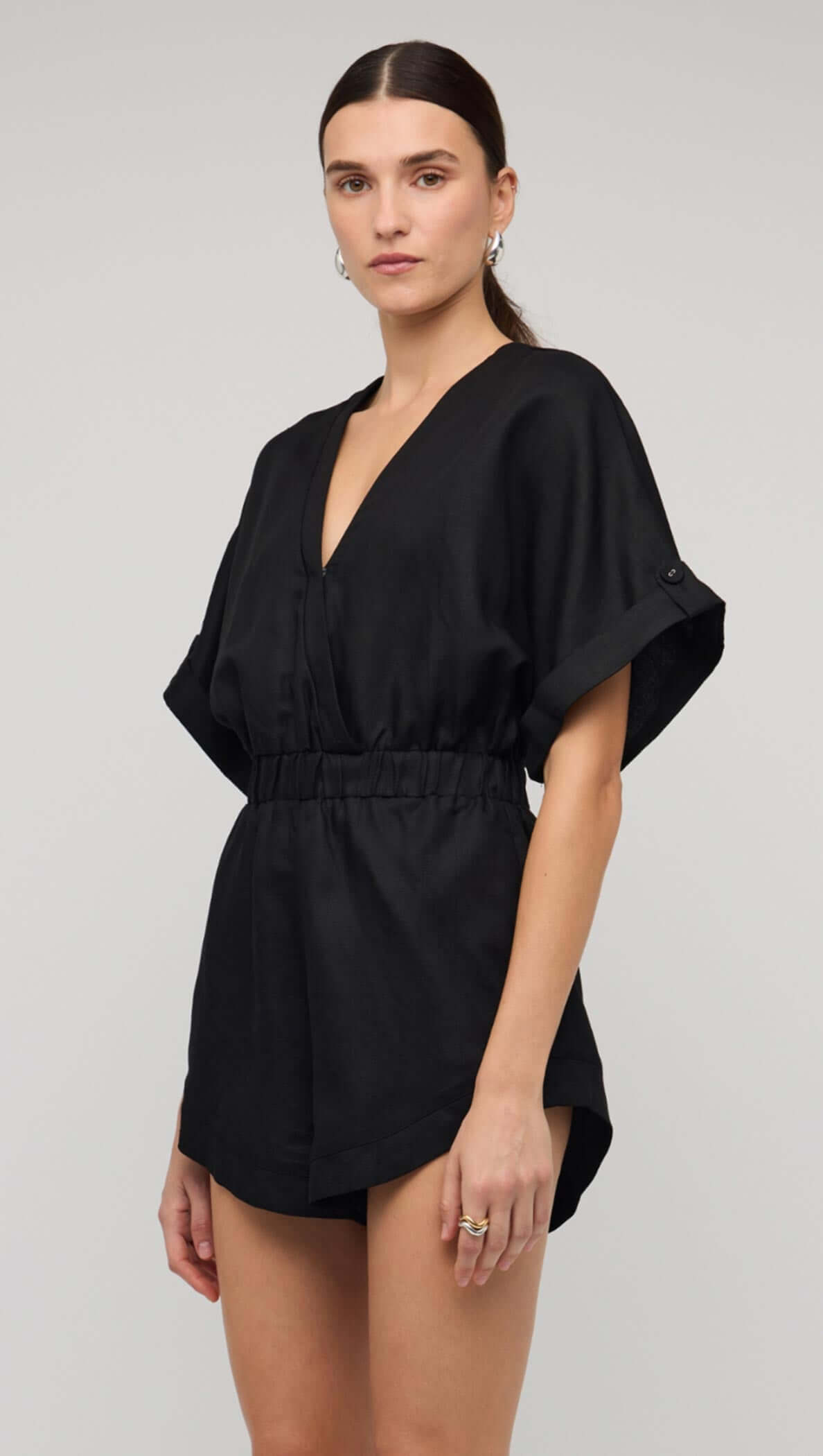 Model wearing a black linen blend V-neck playsuit with an elastic waist and short sleeves.
