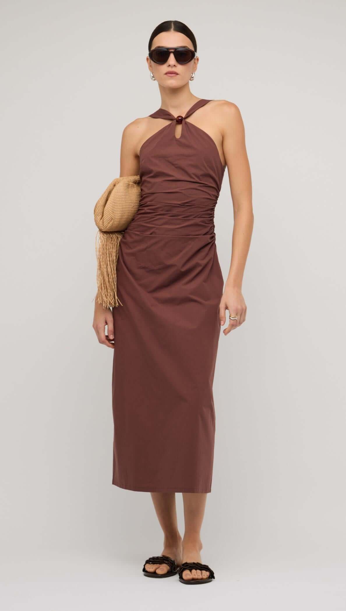 Model wearing a brown cotton bead halter-neck ruched midi dress, accessorized with sunglasses and a clutch.