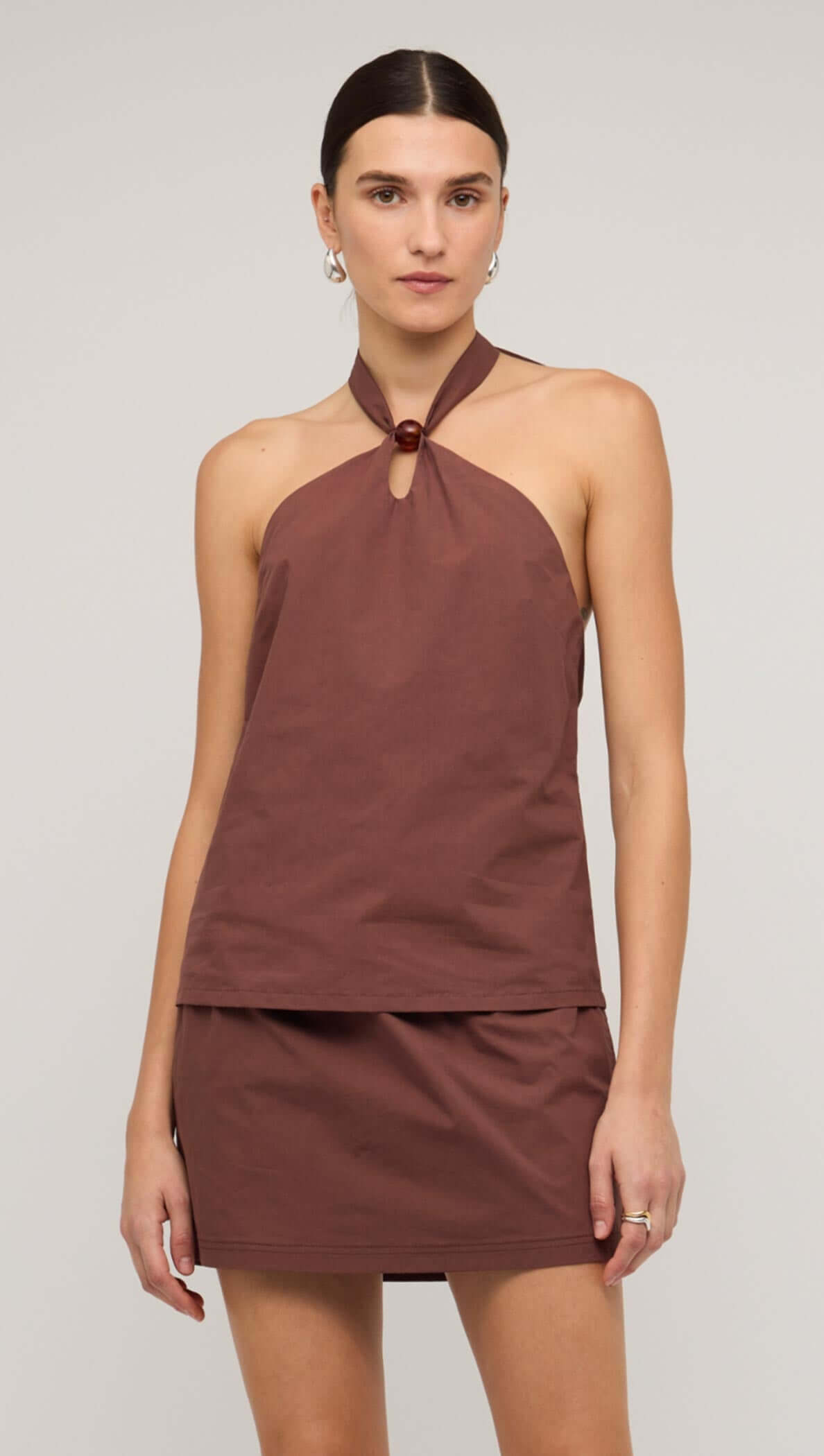 Brown cotton halter-neck top with a minimalist design, featuring a button detail and paired with a matching skirt.