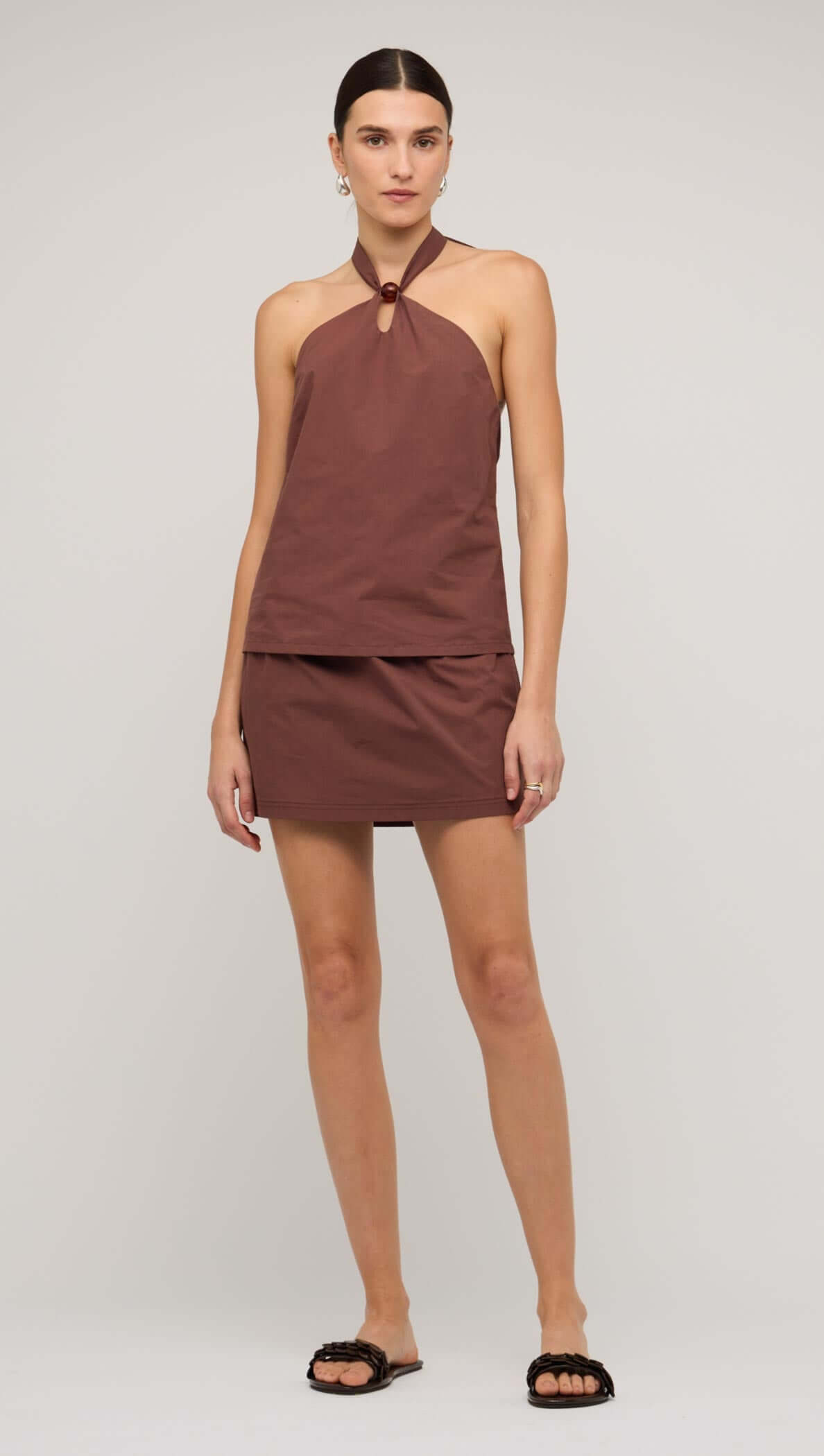 Brown cotton halter-neck top with a minimalist design, featuring a button detail and paired with a matching skirt.