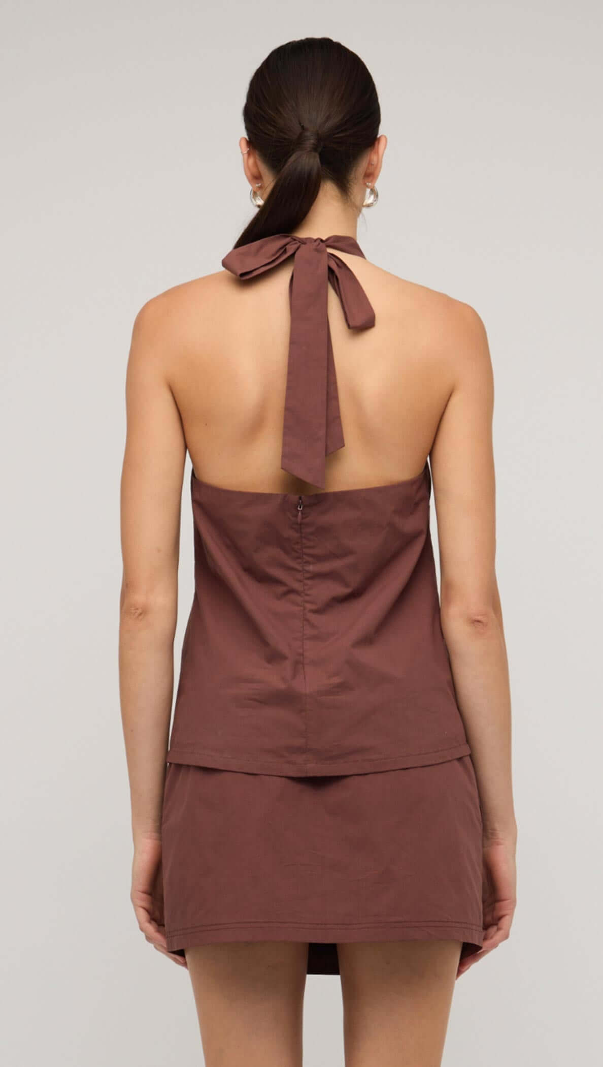Back view of a brown cotton halter-neck top with a tie detail, showcasing a minimalist design and sleek silhouette.