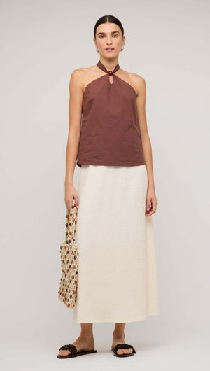 Model wearing a brown cotton halter-neck top with a white skirt, showcasing a chic and minimalist outfit.
