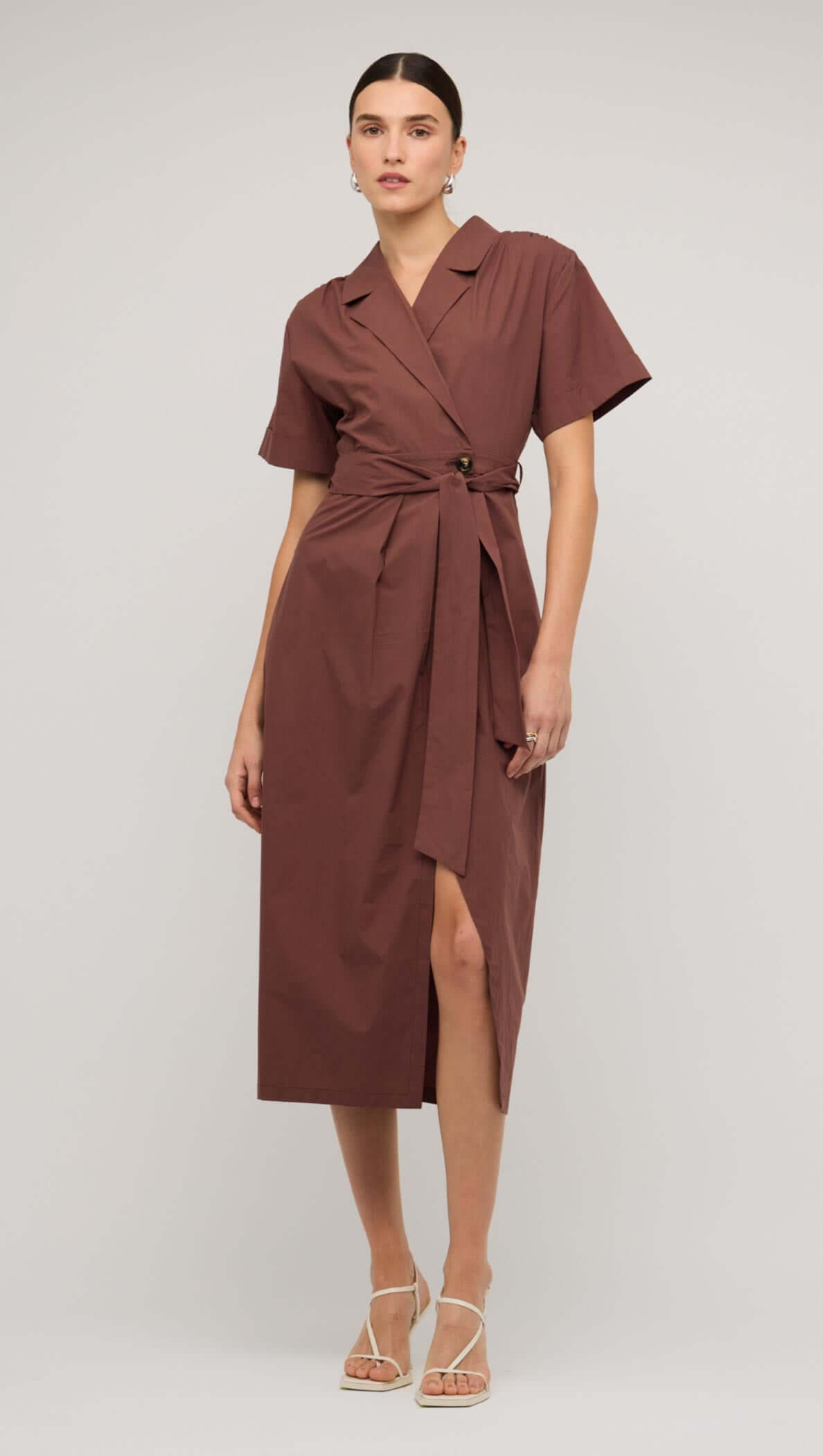 Brown cotton wrap midi shirt dress with short sleeves and a side slit, styled with elegant heels.
