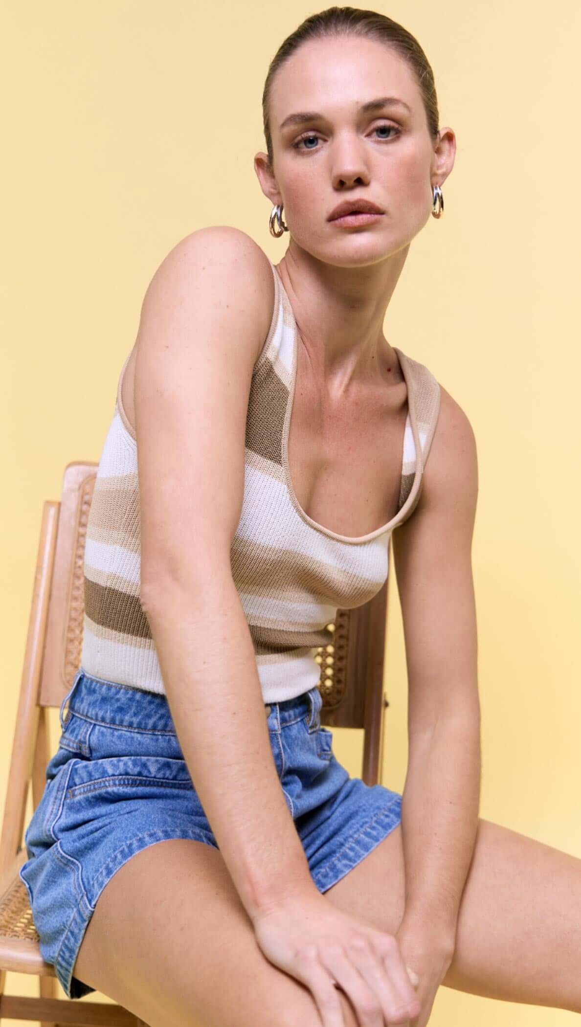 Model wearing a Reversible Stripe Knit Tank paired with denim shorts against a yellow background.