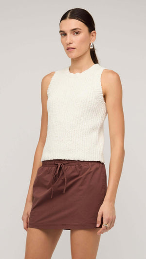 Model wearing a white knit tank top paired with a brown drawstring skirt, showcasing modern casual style.