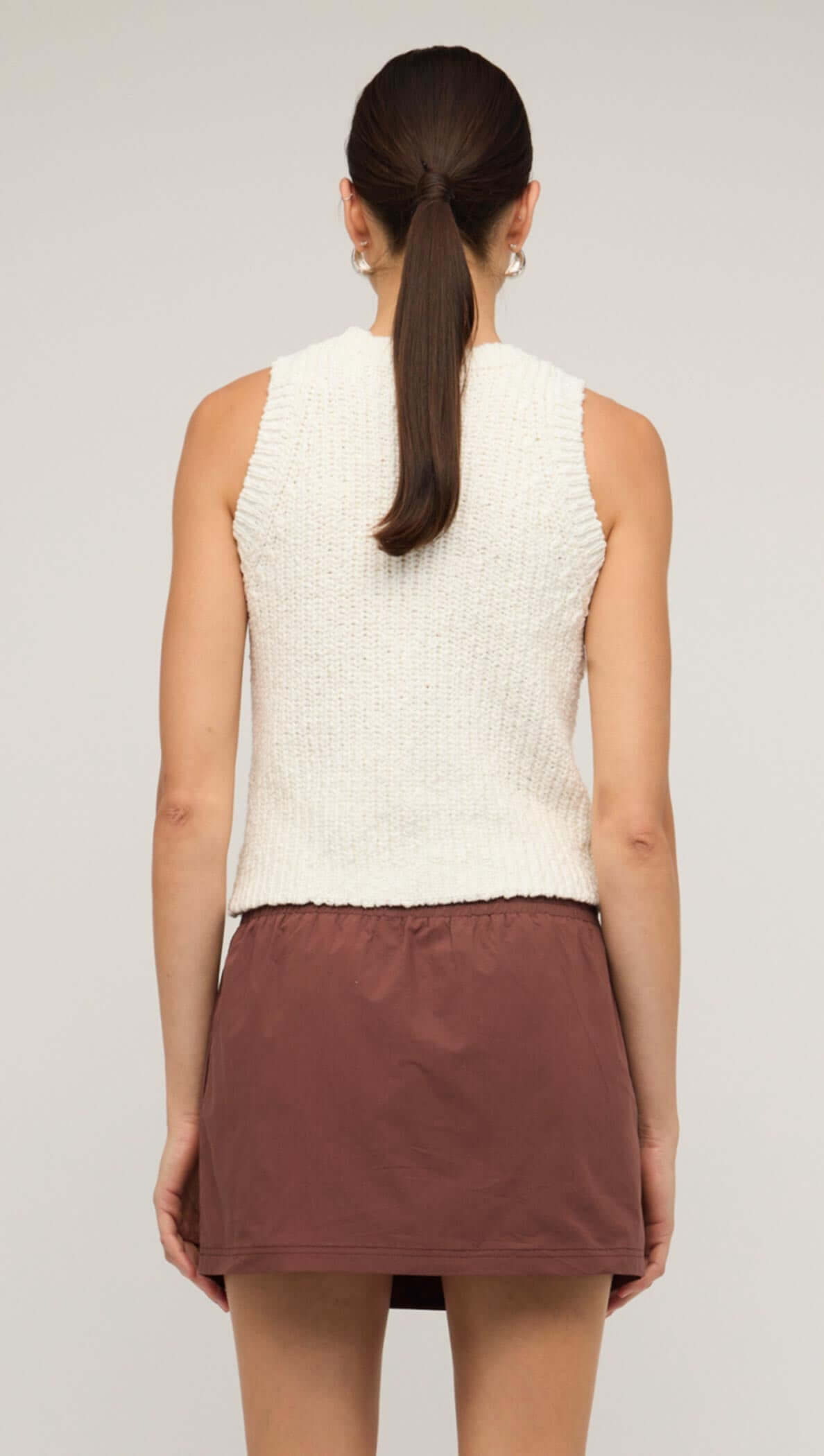 Back view of a woman wearing a white knit tank top with a brown skirt, showcasing a comfortable and stylish layering piece.