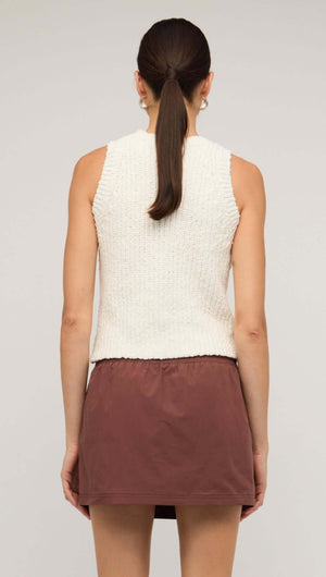 Back view of a woman wearing a white knit tank top with a brown skirt, showcasing a comfortable and stylish layering piece.