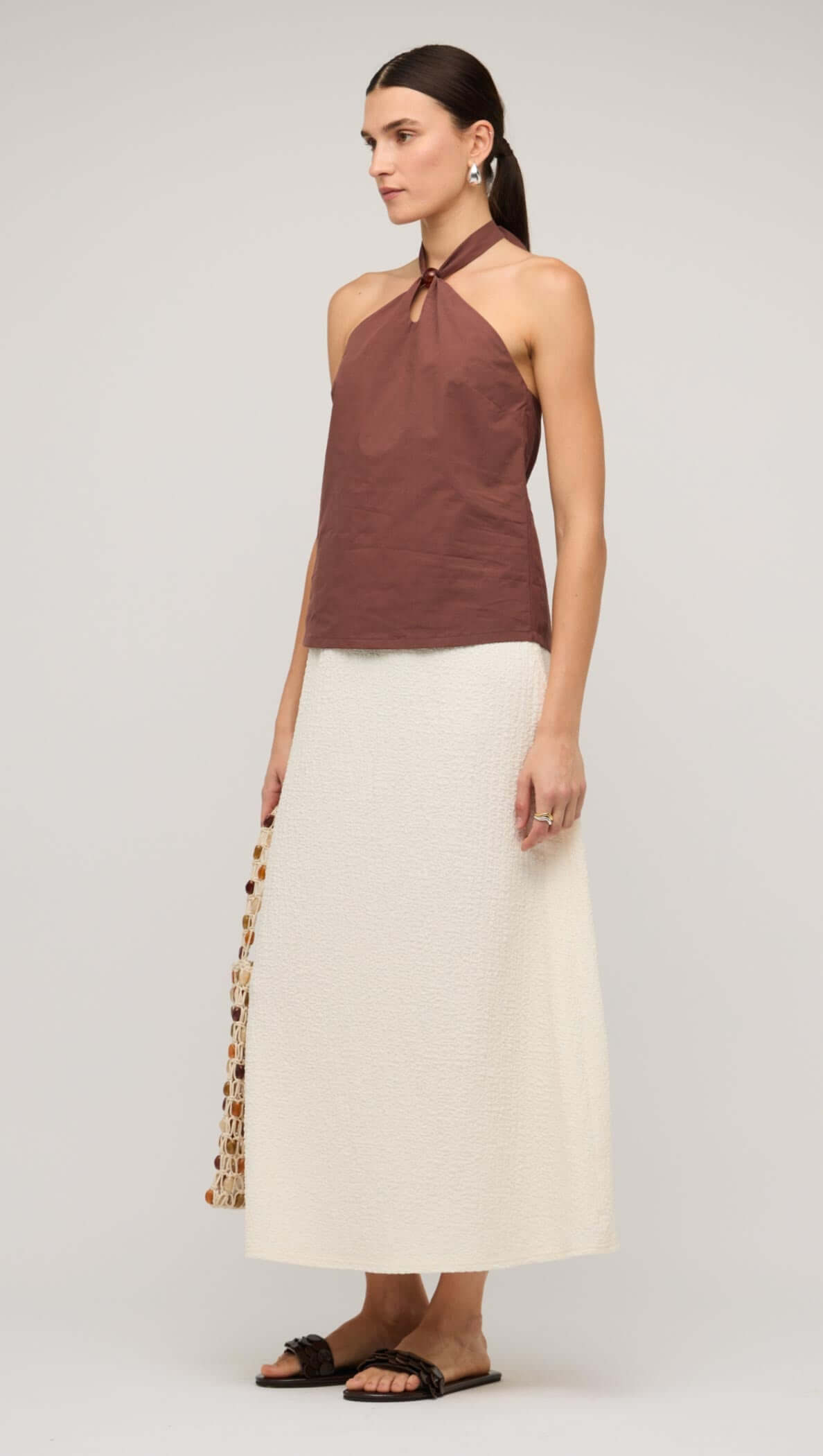 Model showcasing a cream A-line midi skirt paired with a brown halter top and sandals.