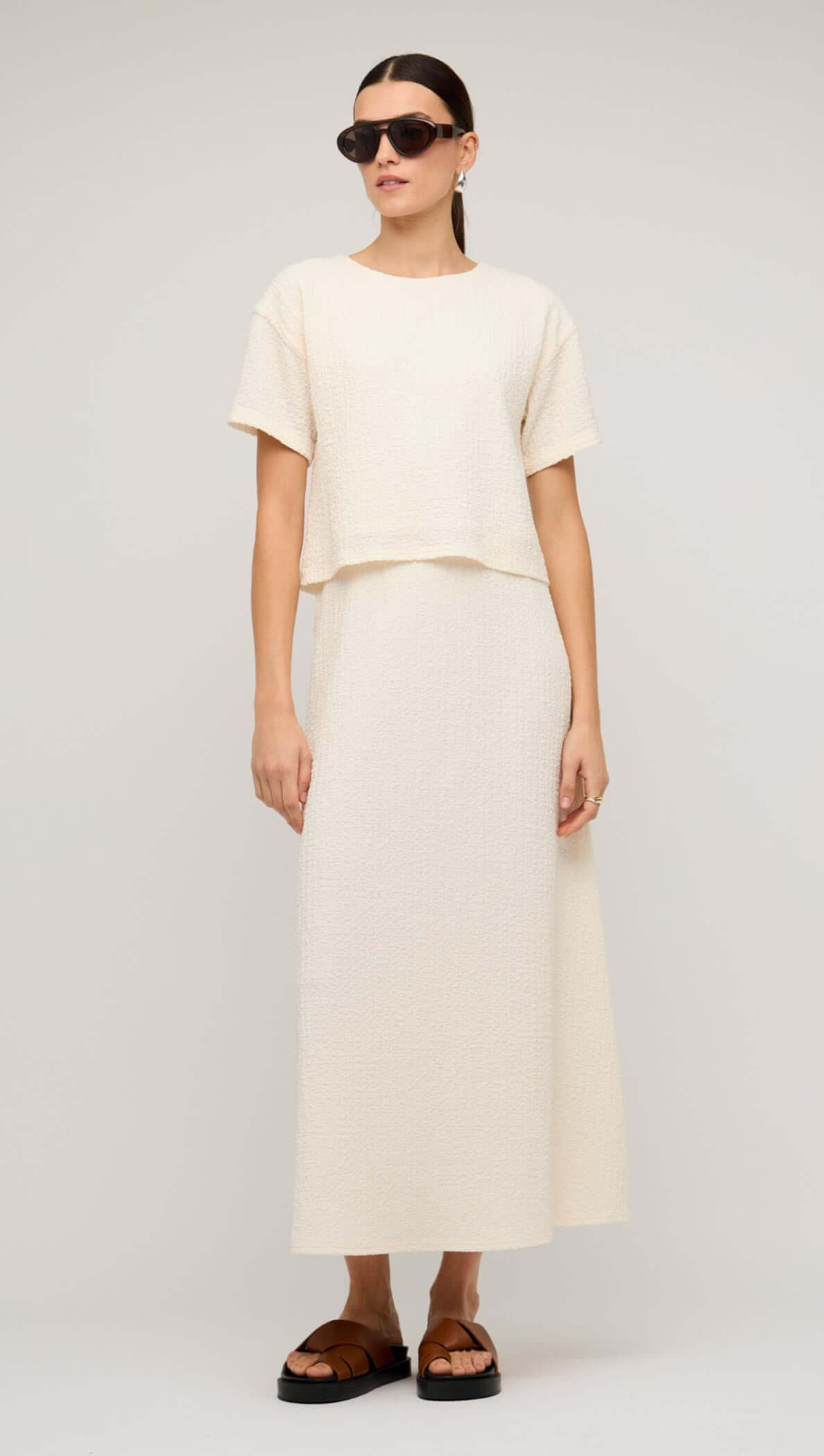 Model wearing a cream boxy short sleeve cropped top with a matching maxi skirt and stylish sunglasses.