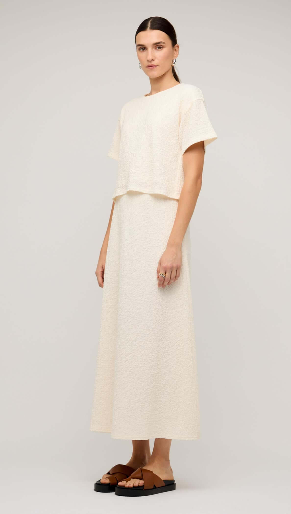 Model wearing a cream boxy short sleeve cropped top paired with a long skirt and flat sandals.