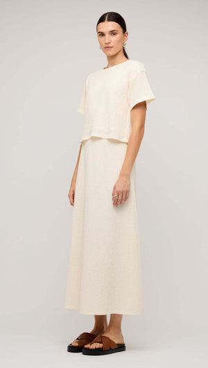 Model wearing a cream boxy short sleeve cropped top paired with a long skirt and flat sandals.