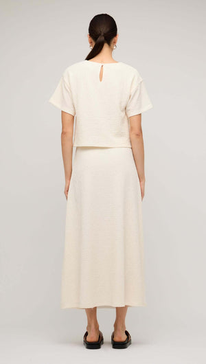 Back view of a model wearing a cream boxy short sleeve cropped top paired with a matching long skirt.