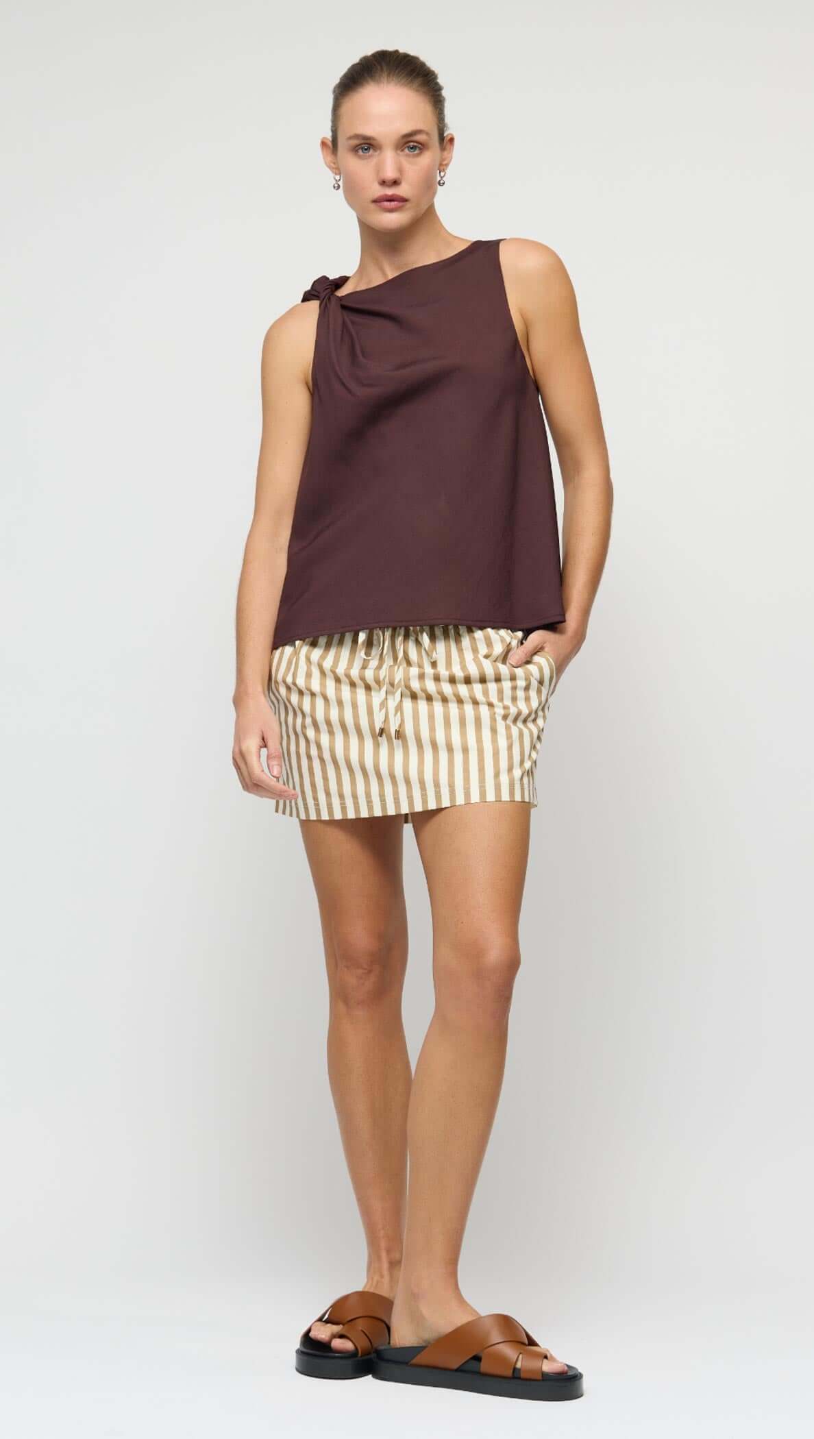 Model showcasing the Elira Chocolate Twist Top with shoulder knot detail and relaxed fit paired with striped shorts.