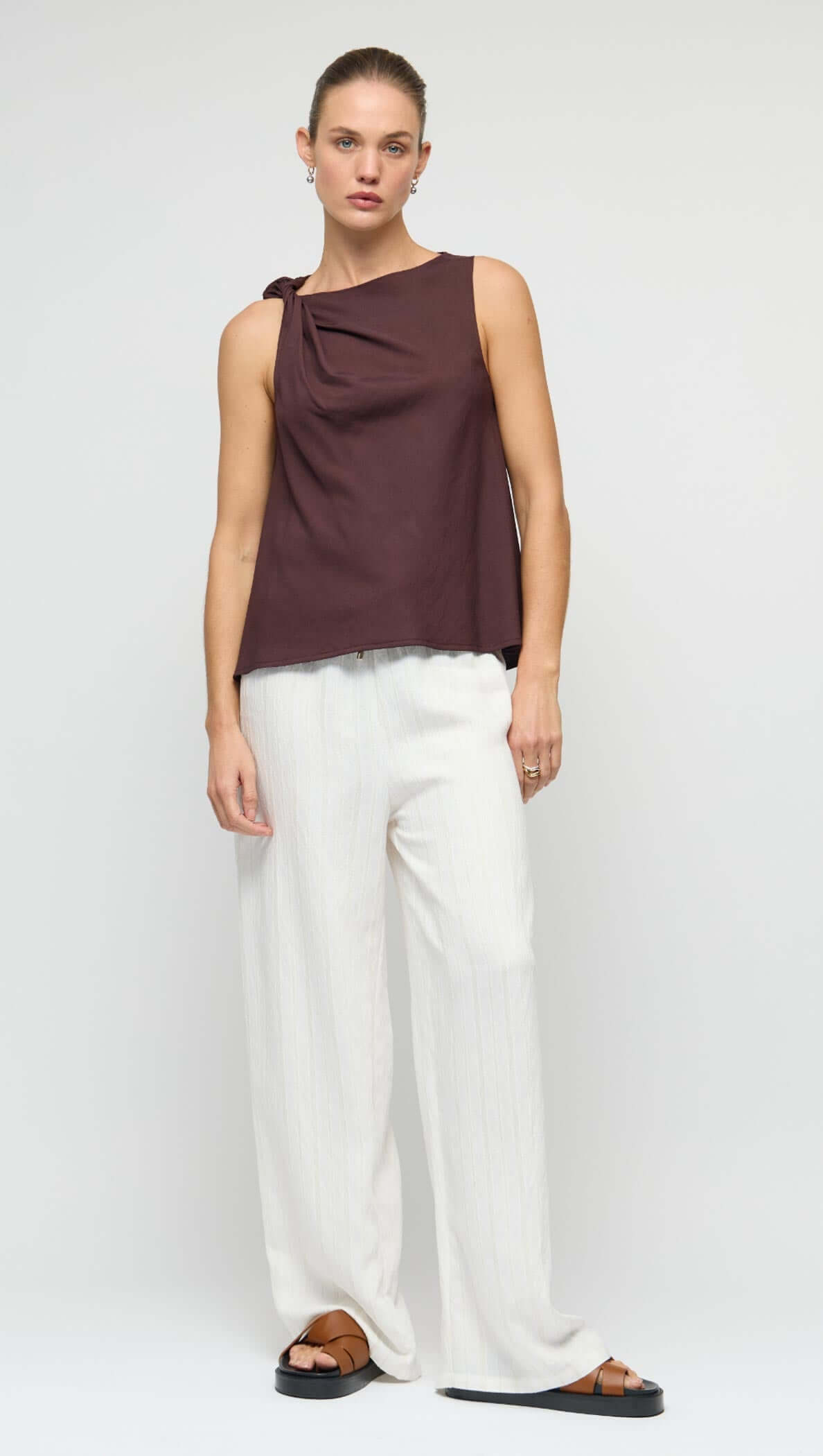 Model wearing a Chocolate Twist Top with shoulder knot detail, paired with white wide-leg pants, showcasing a relaxed fit.