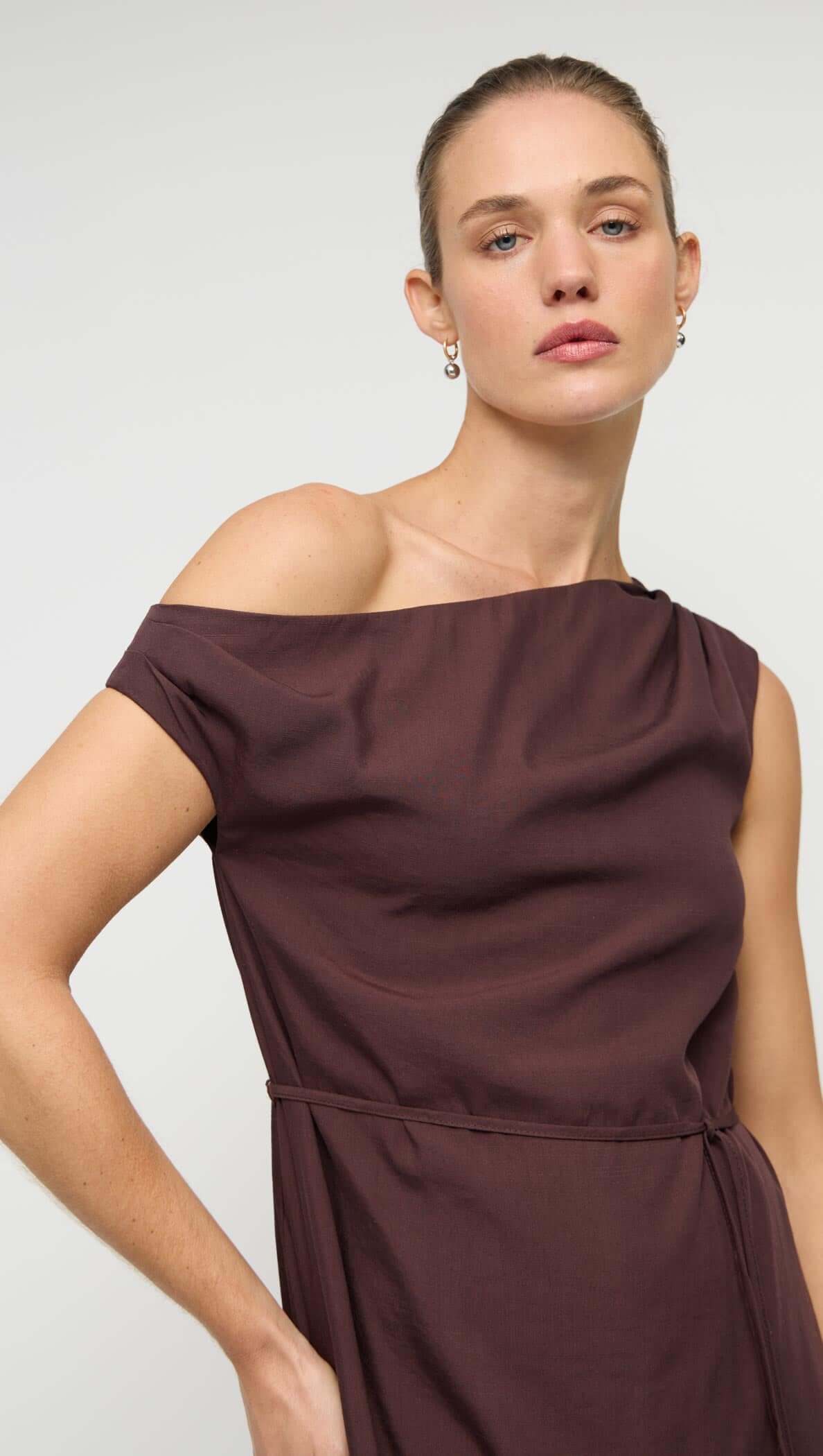 Linen Blend Chocolate Asymmetrical Mini Dress on a model showcasing its unique one-shoulder design and self-tie bow detail.