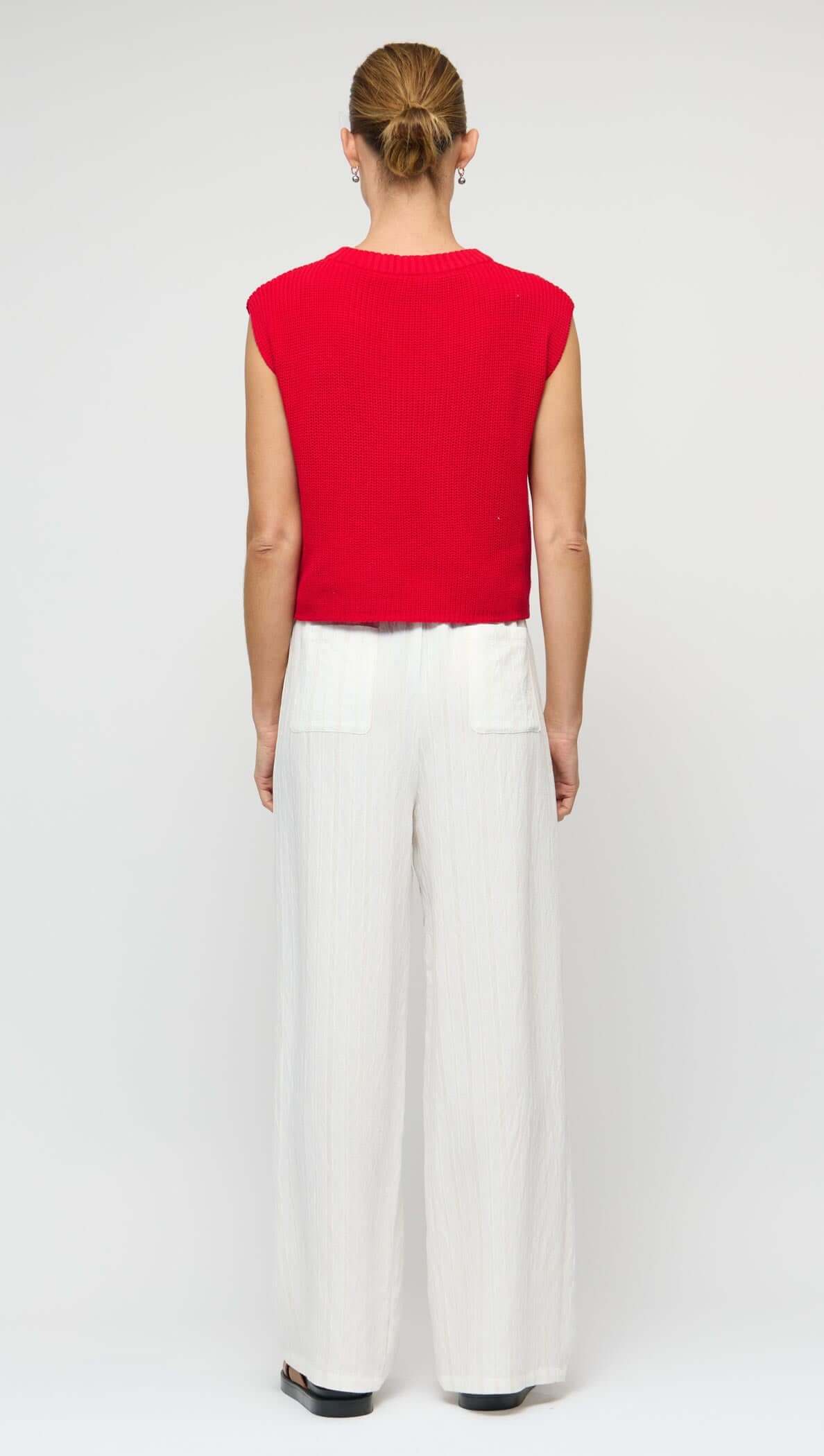 Back view of a model wearing a Cotton Blend Red Knit Tank Top with white wide-leg pants.