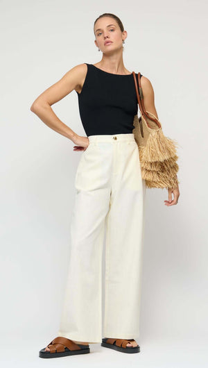 Model wearing a Reversible Black Knit Tank Top with wide white pants and a straw bag.