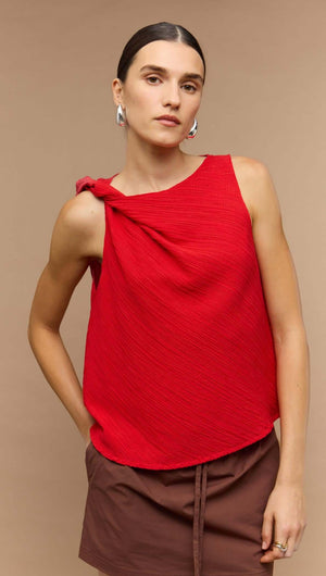 Model wearing a vibrant red crepe twist top, featuring a stylish knot detail, paired with brown shorts.