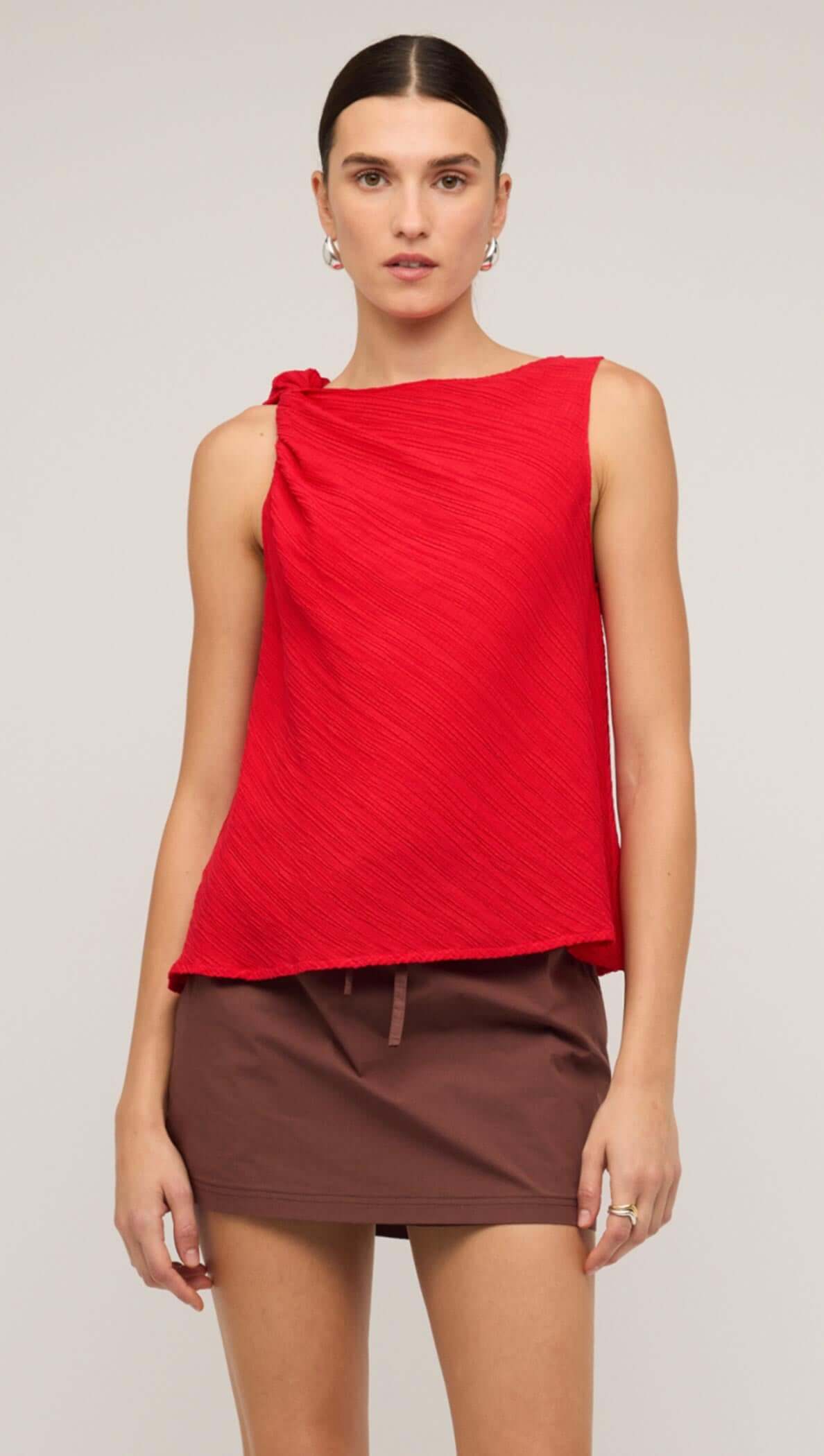 Model wearing a stylish red crepe twist top paired with a brown mini skirt, showcasing modern fashion.