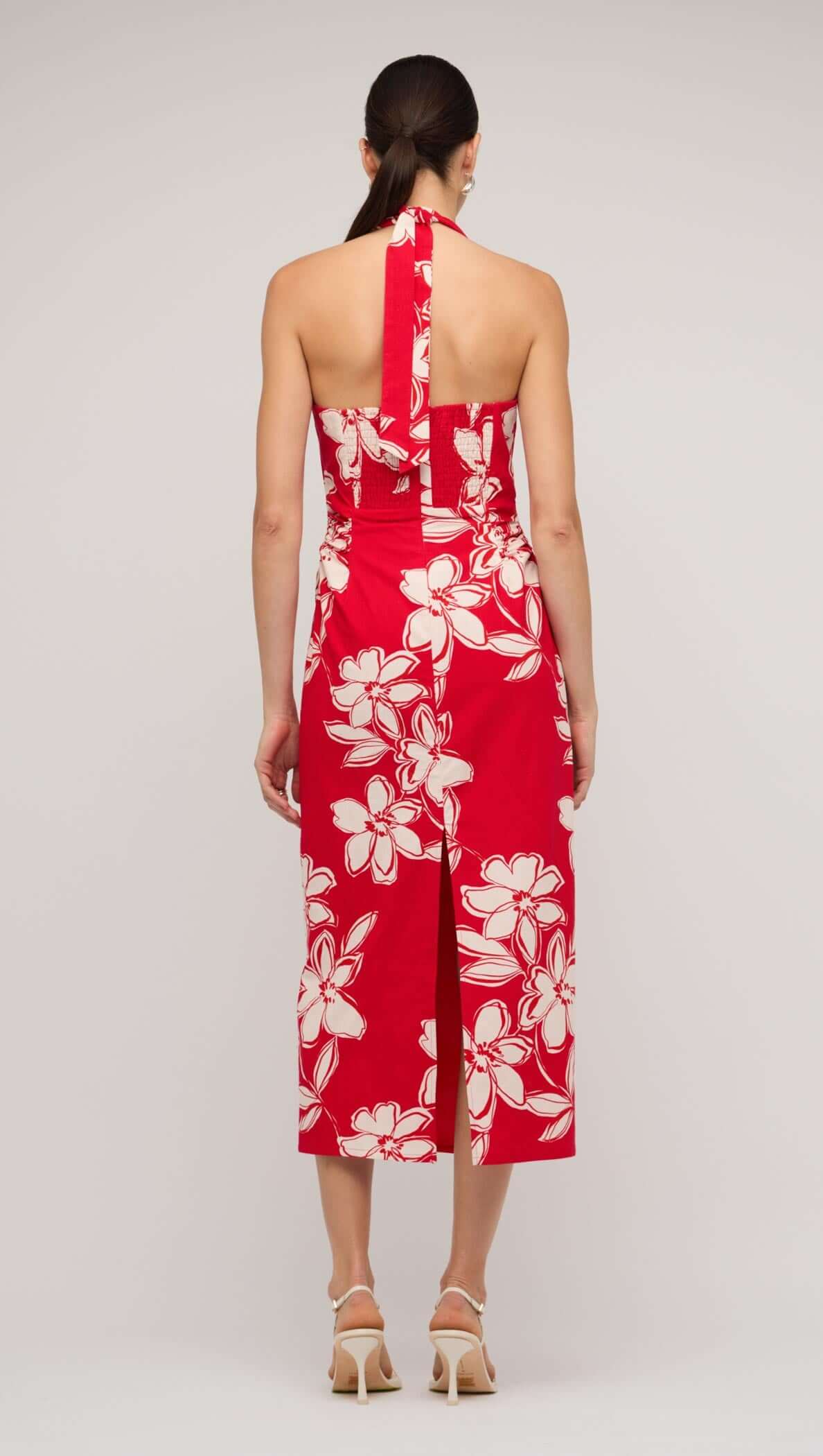 Back view of a red and white floral halter-neck midi dress with a slit, showcasing elegant summer fashion.