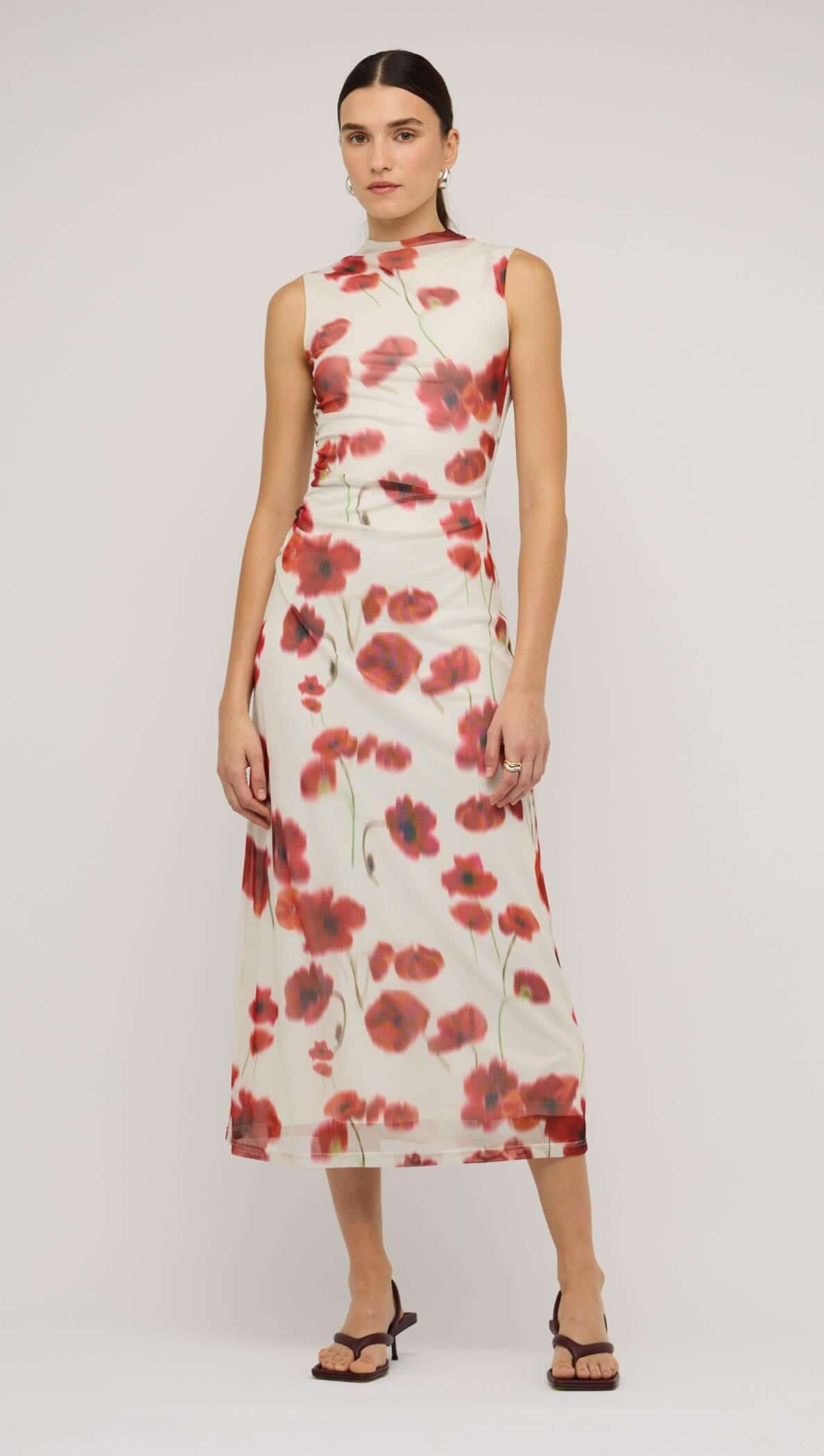 Model wearing a red and white poppy print mesh midi dress against a red background, showcasing a stylish side view.
