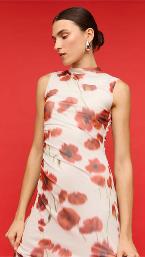 Woman in a sleeveless red and white poppy print mesh midi dress against a vibrant red background.
