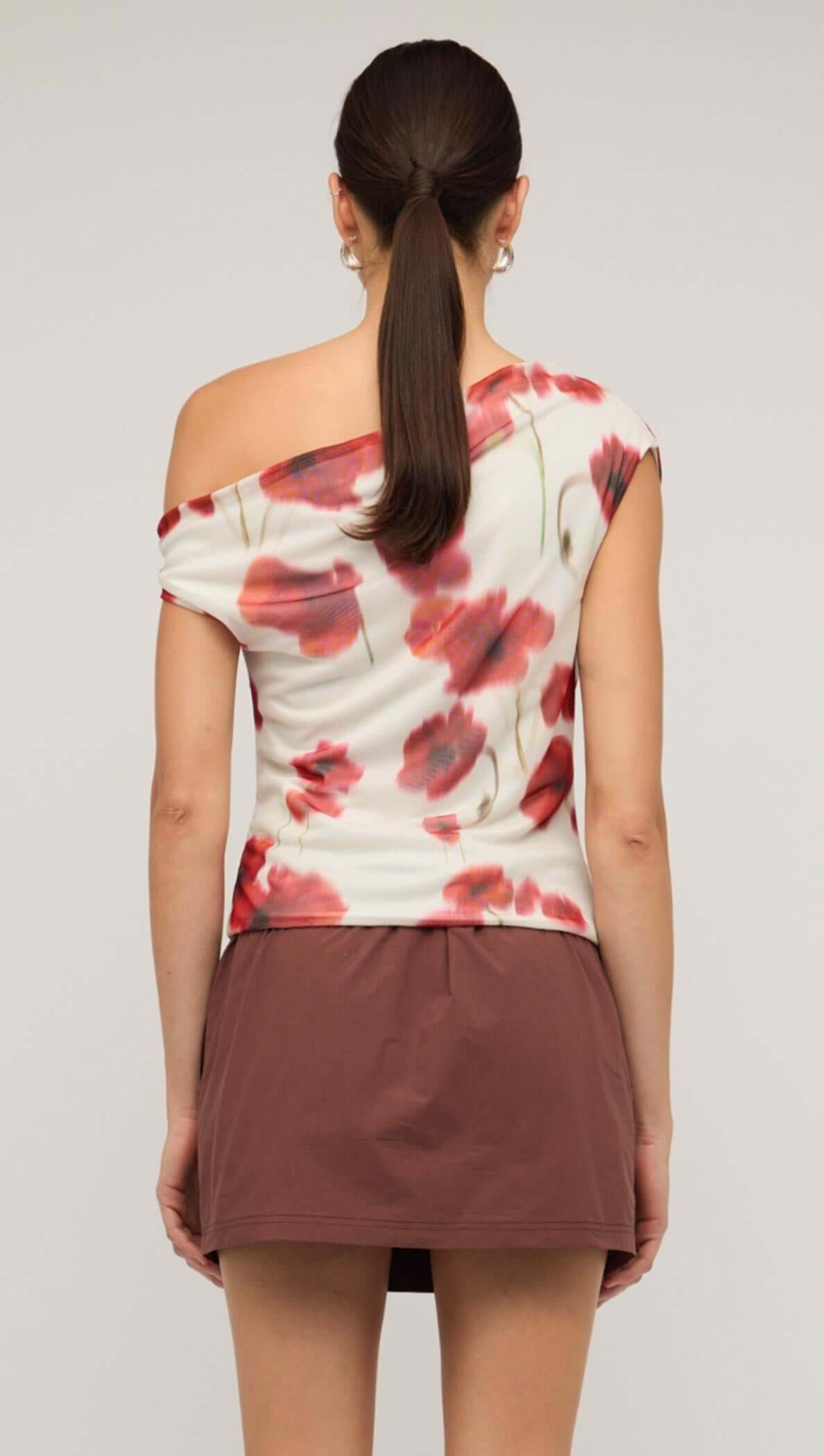 Back view of a red and white poppy print off-shoulder mesh top, paired with a brown mini skirt.