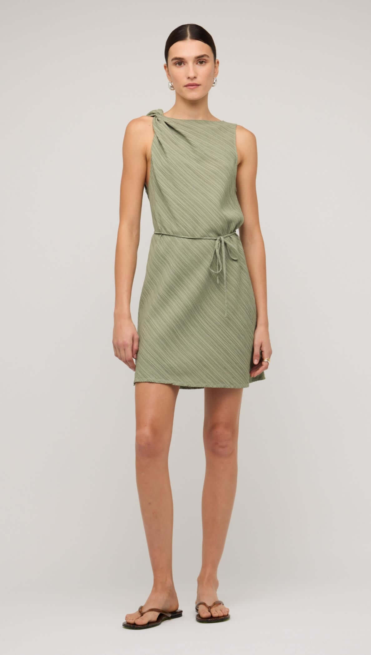 Sage green mini dress with tie waist, featuring a one-shoulder design and textured fabric.