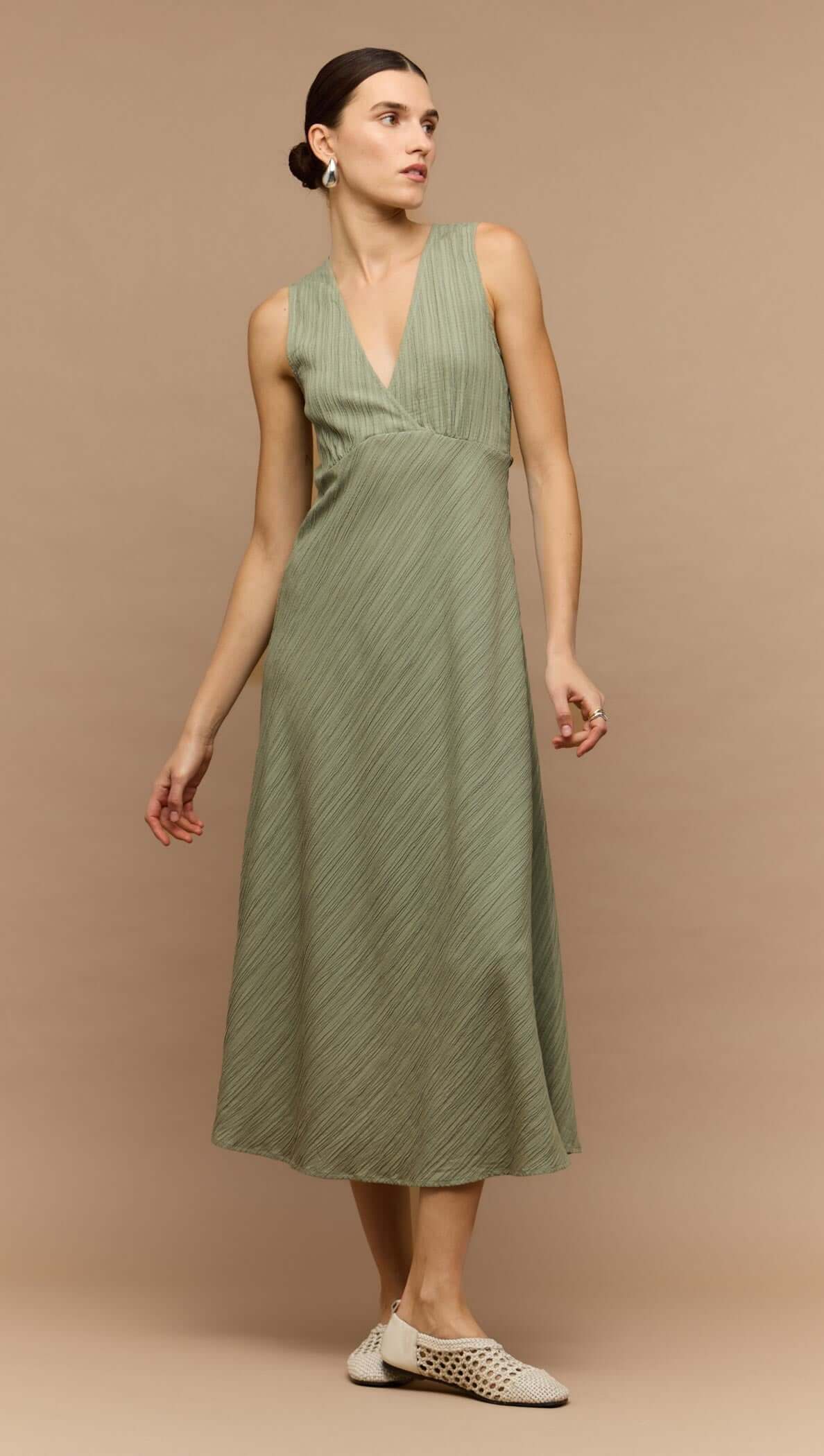 Model wearing a sage green v-neck bias midi dress, featuring a sleek design and elegant silhouette.