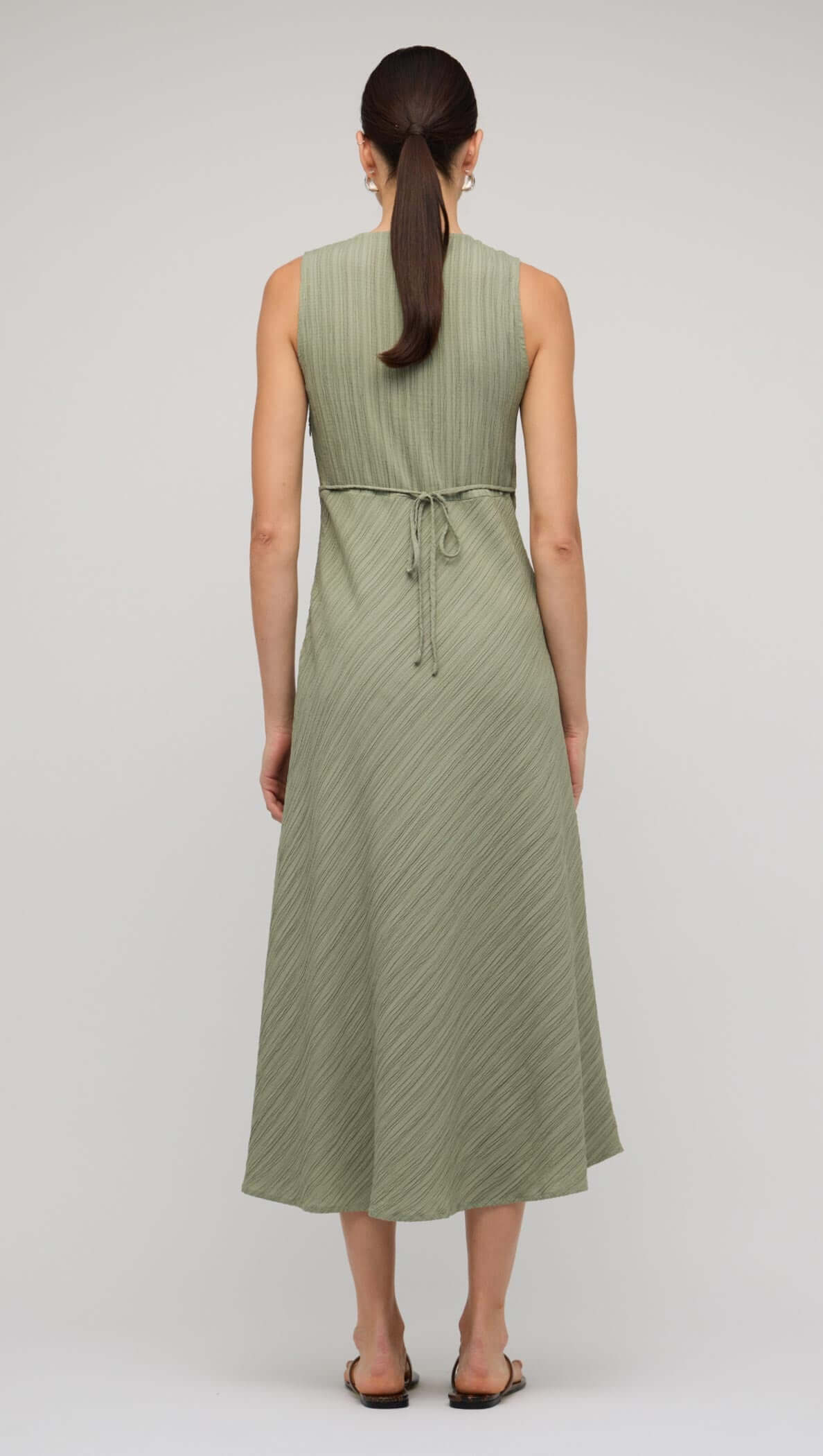 Back view of a sage green V-neck bias midi dress showcasing its elegant fit and tie detail.