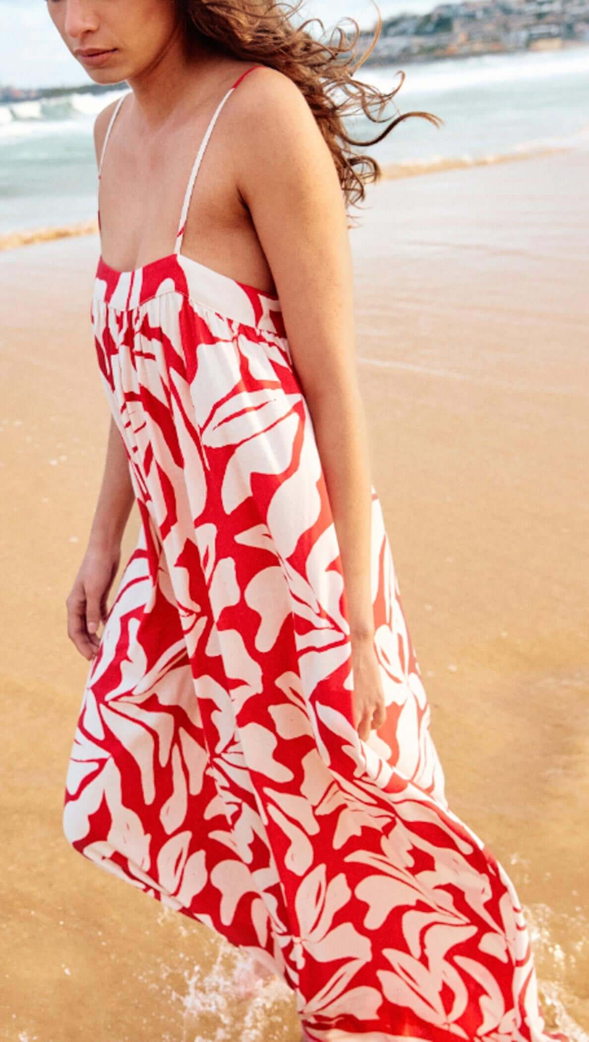 Woman wearing a Cotton Blend Red & White Floral Print Maxi Dress while walking on the beach.
