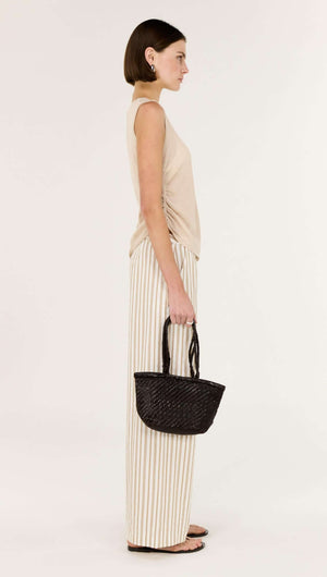 Side view of a model wearing a Sheer Drawstring Knit Tank Top with striped wide-leg pants and a small black bag.