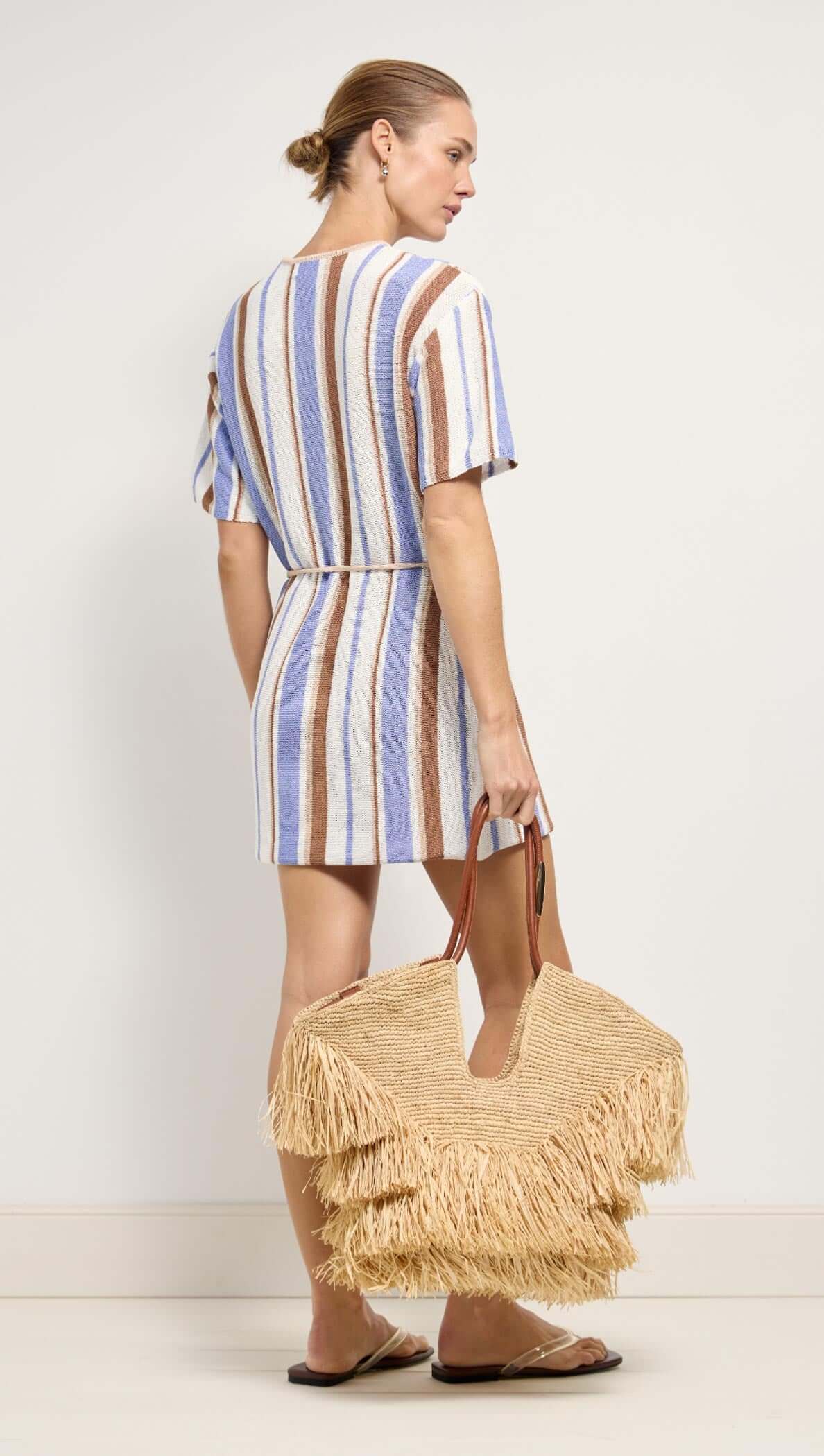 Model wearing Striped Knit T-Shirt Mini Dress with a straw bag, showcasing a relaxed and stylish coastal look.