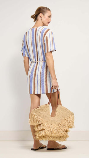 Model wearing Striped Knit T-Shirt Mini Dress with a straw bag, showcasing a relaxed and stylish coastal look.