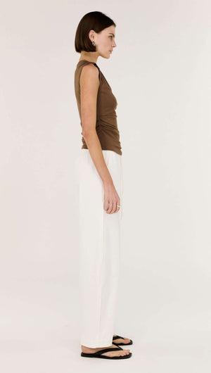 Model wearing Brown Ruched Slinky Tank in brown with white pants, showcasing its sleek design and shoulder detail.