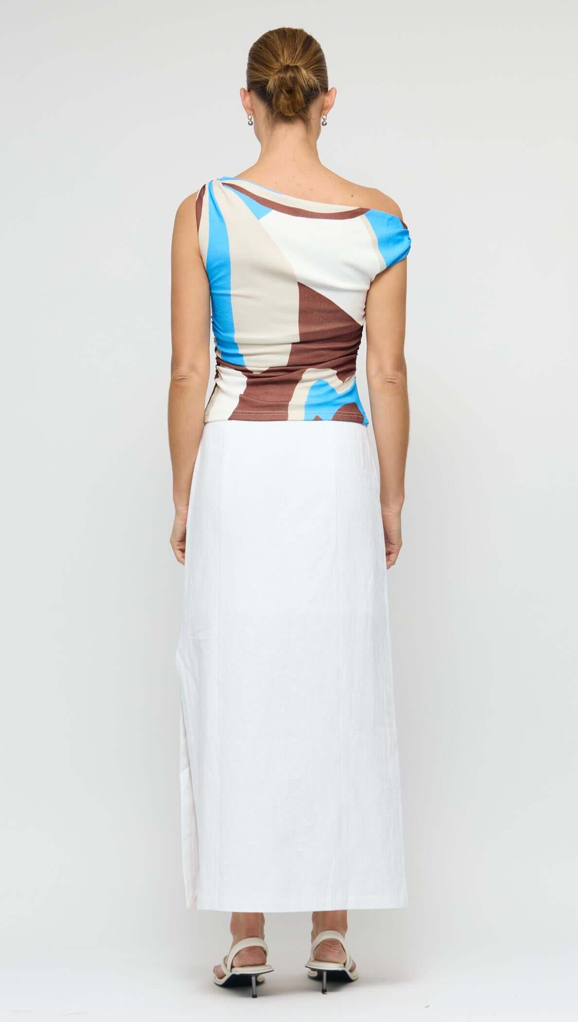 Back view of a model wearing a Blue Abstract Asymmetric Mesh Top with a long white skirt.