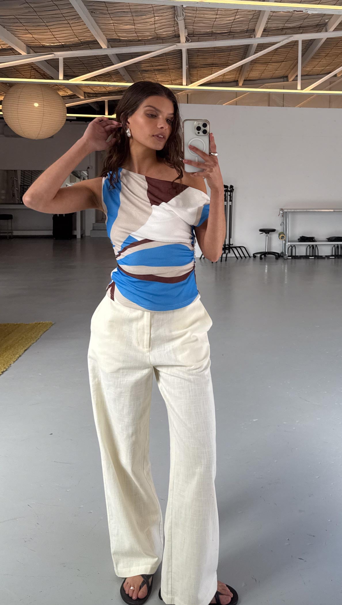 Blue Abstract Asymmetric Mesh Top worn by model, showcasing abstract print with asymmetrical neckline and ruched waist worn with white linen pants.