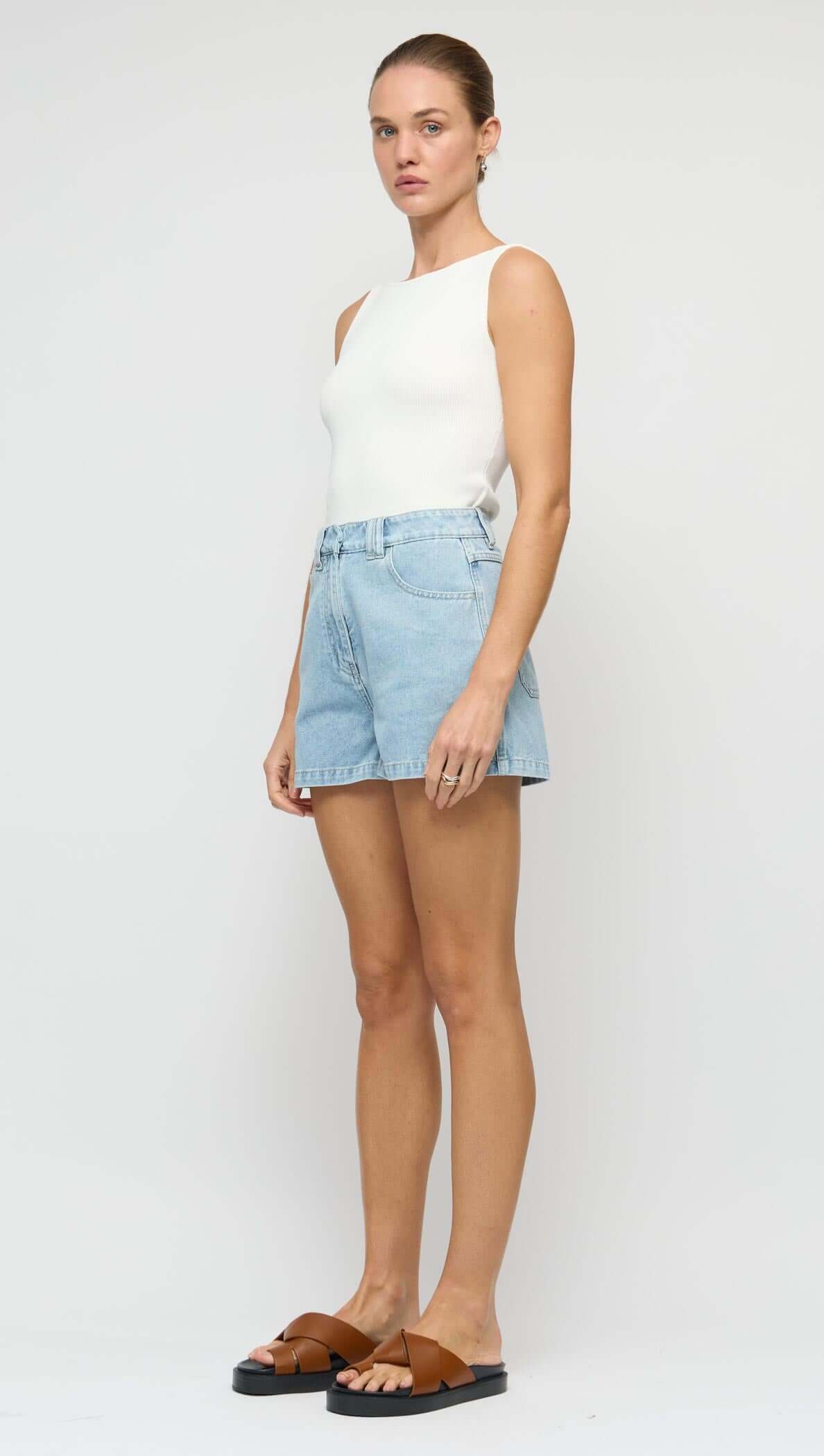 Model wearing a White Reversible Knit Tank Top with blue denim shorts and brown sandals on a neutral background.