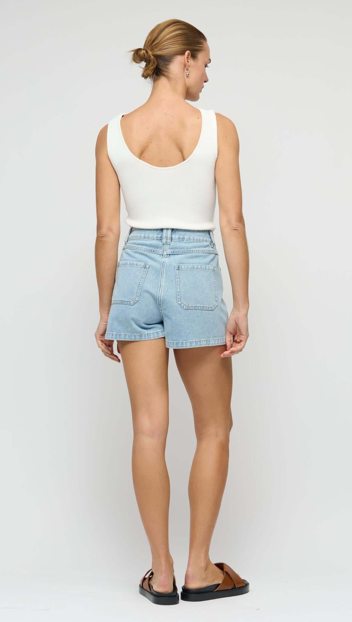 Back view of a model wearing a White Reversible Knit Tank Top with denim shorts, showcasing a casual summer look.